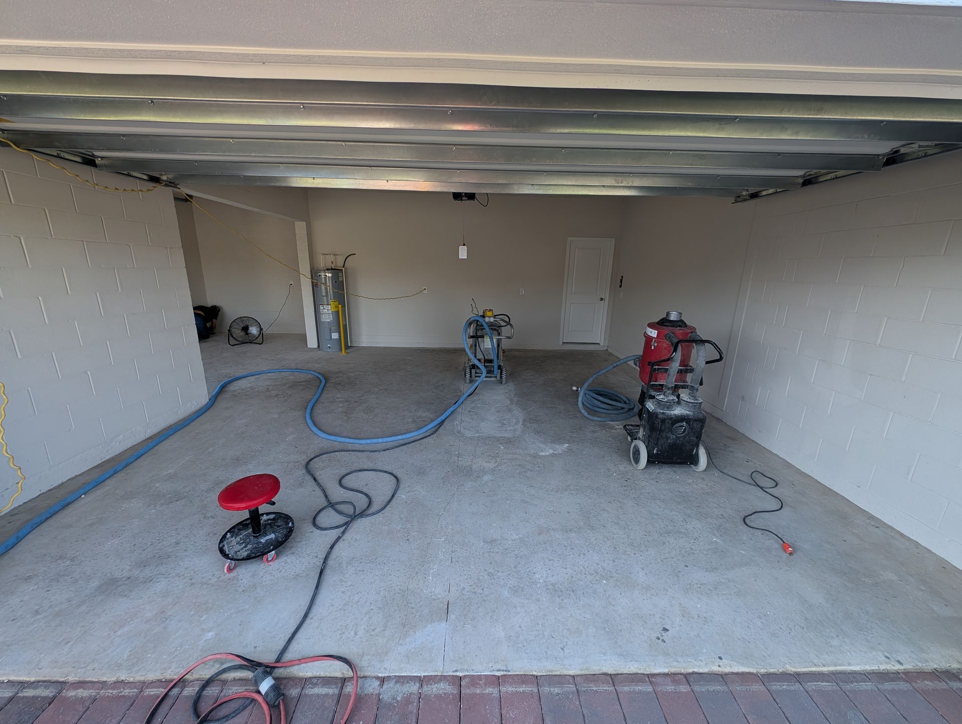 Empty garage under renovation with tools, hoses, and equipment on the concrete floor
