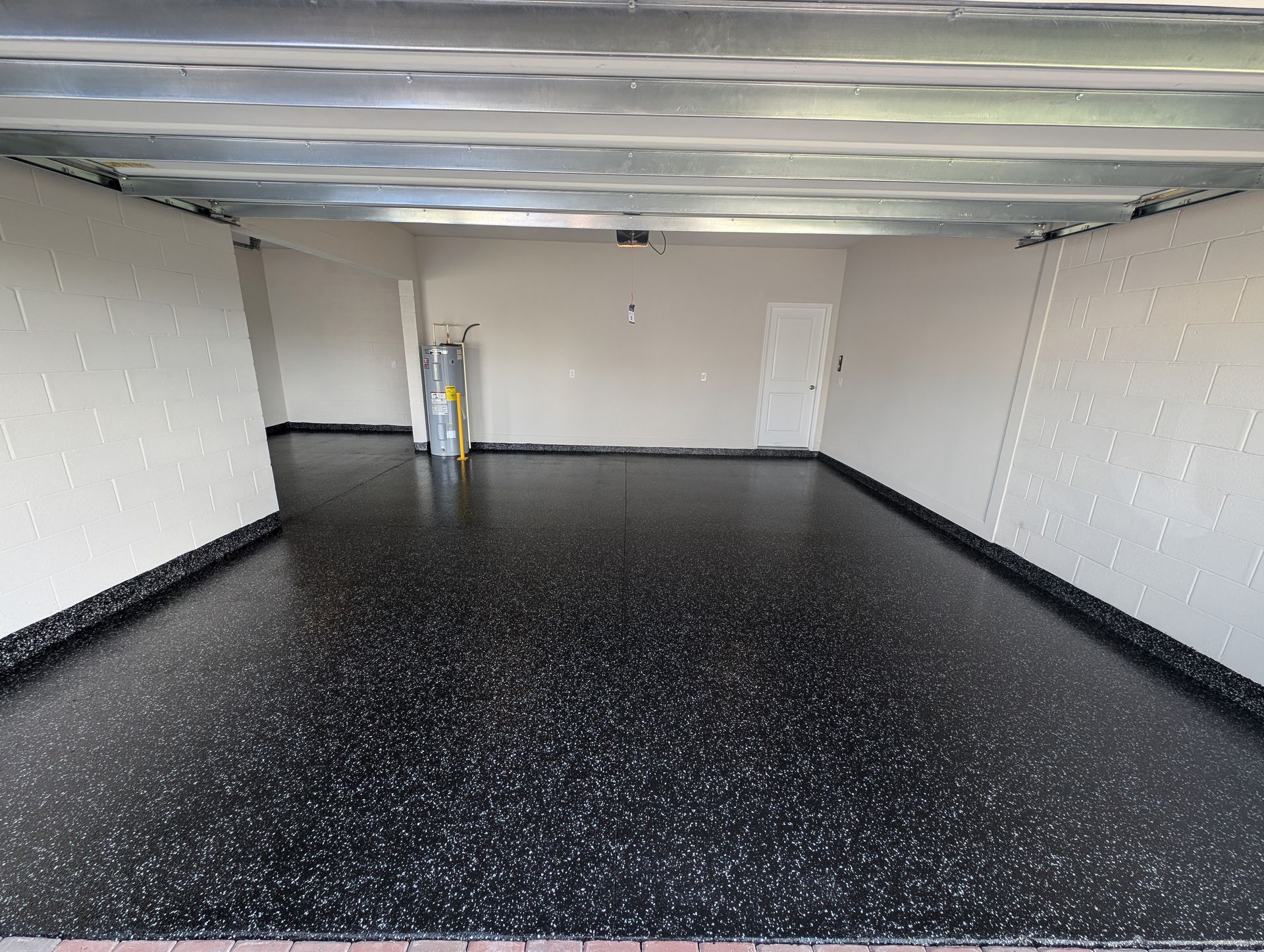 Empty garage with black speckled floor, white walls, and a partially visible ladder near the back wall