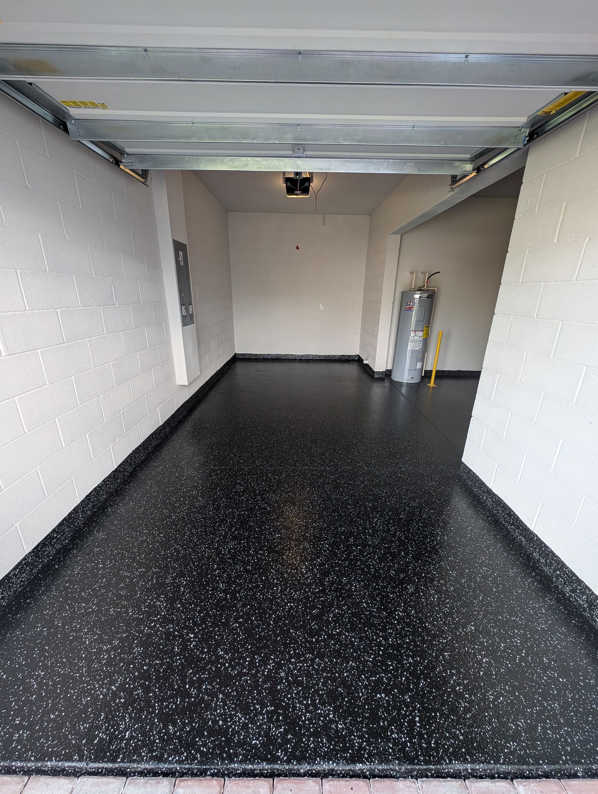 Empty garage with black speckled floor, white walls, and a closed overhead door.