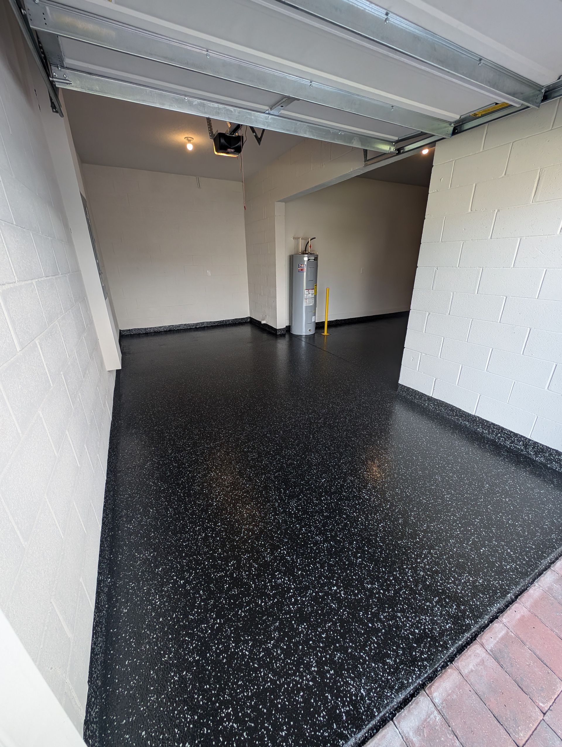 Empty garage with black speckled floor, white walls, and a water heater near the back.