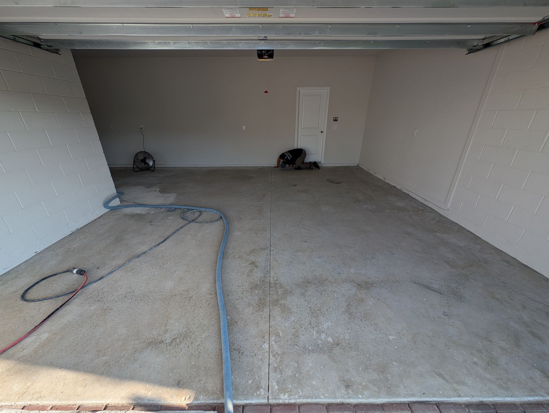 Empty concrete garage interior with open door, gray floor, and a hose on the ground