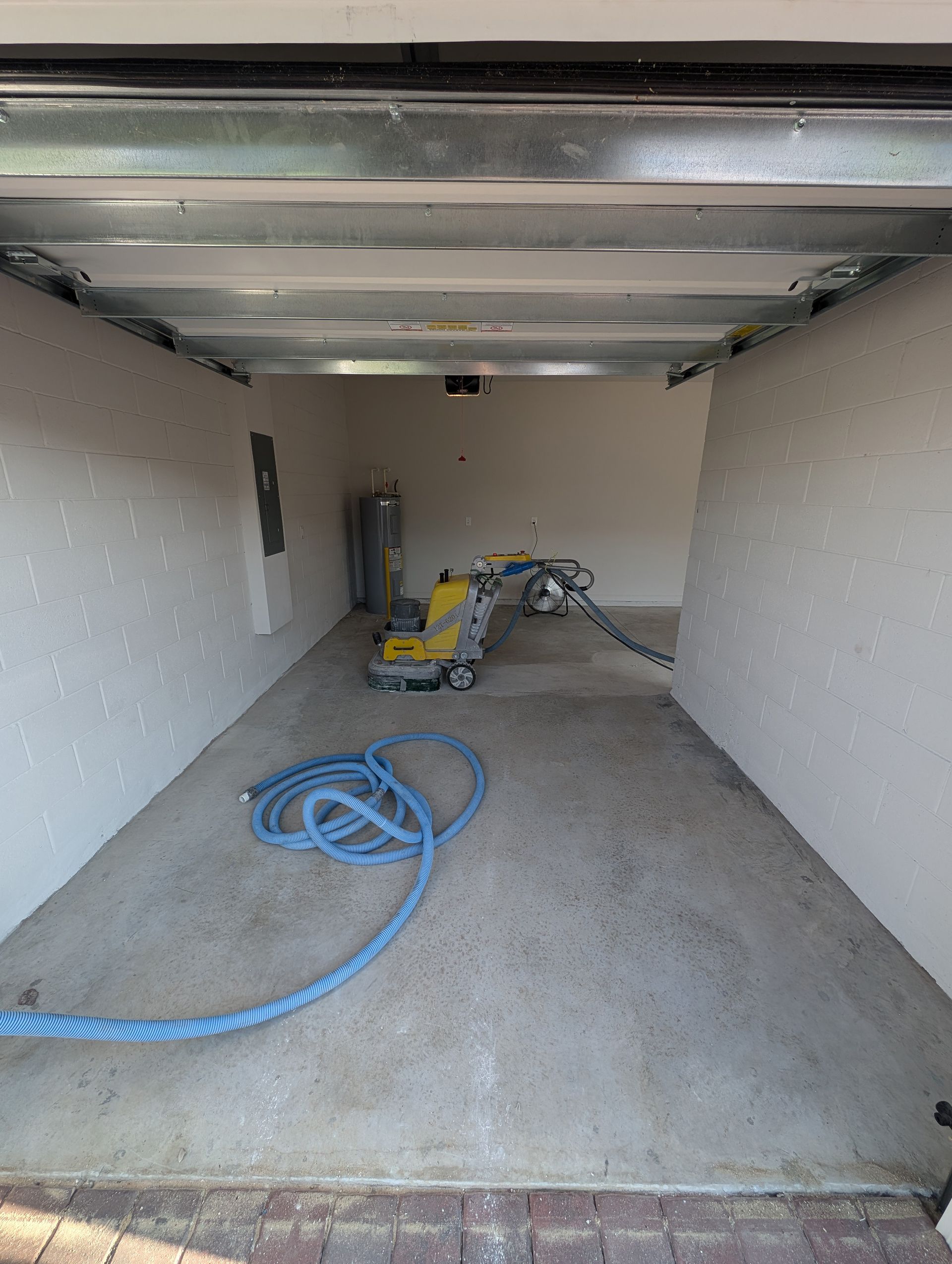 Empty garage with concrete floor, coiled blue hose, and tools near the back wall.
