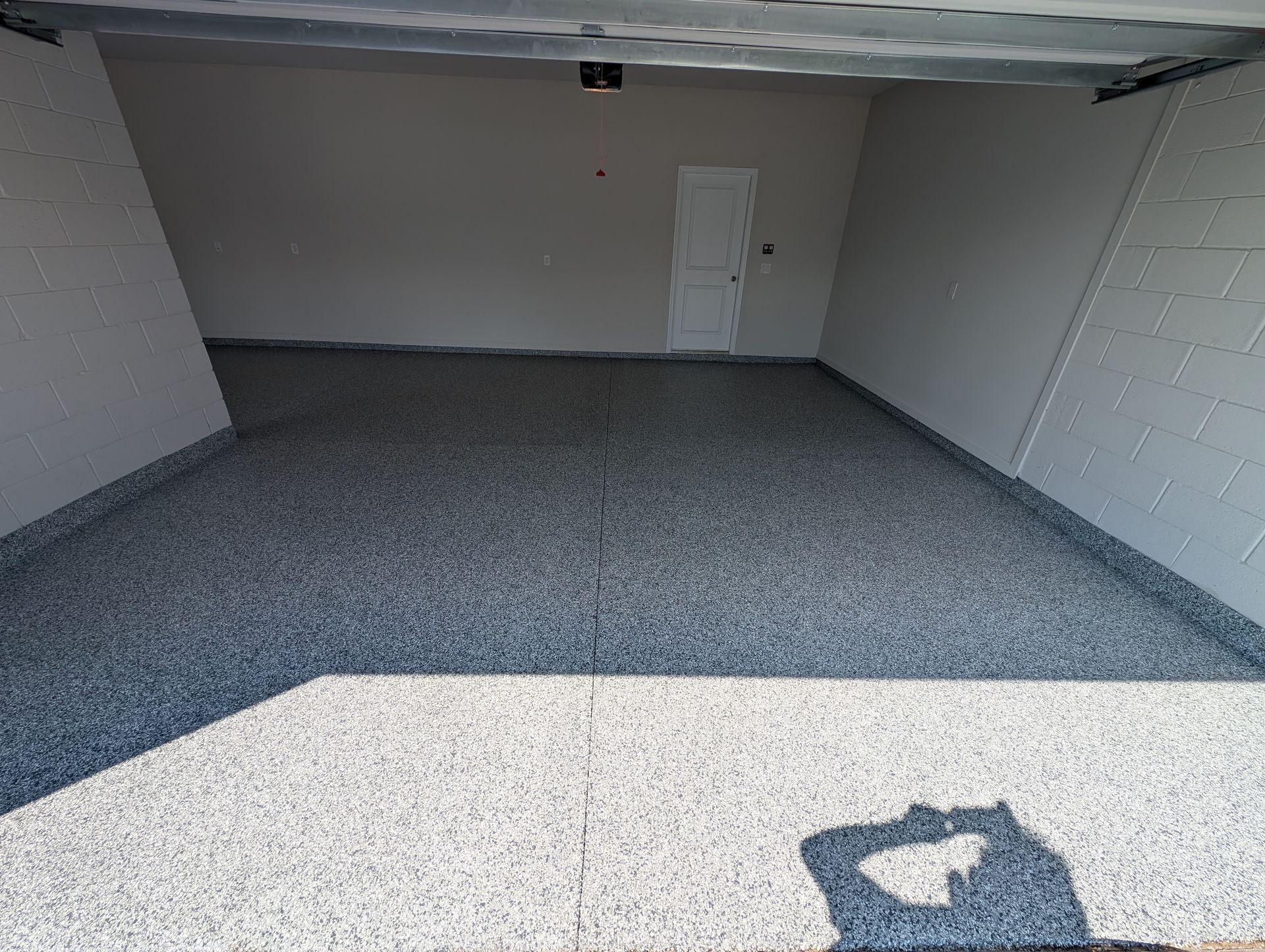 Empty garage with a gray floor, white walls, and a closed door at the back.