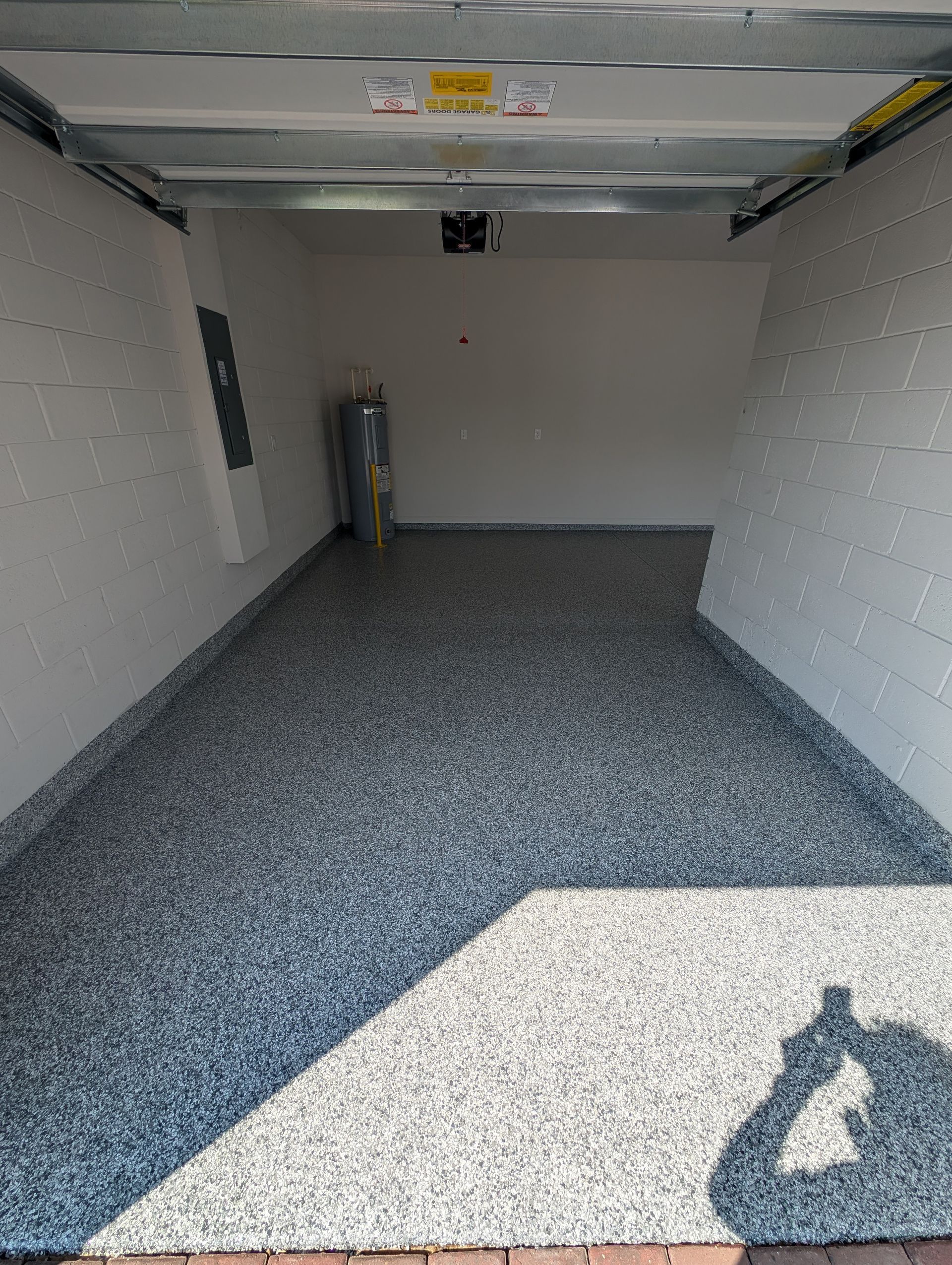 Empty garage with speckled epoxy floor, white walls, and a garage door open to daylight.