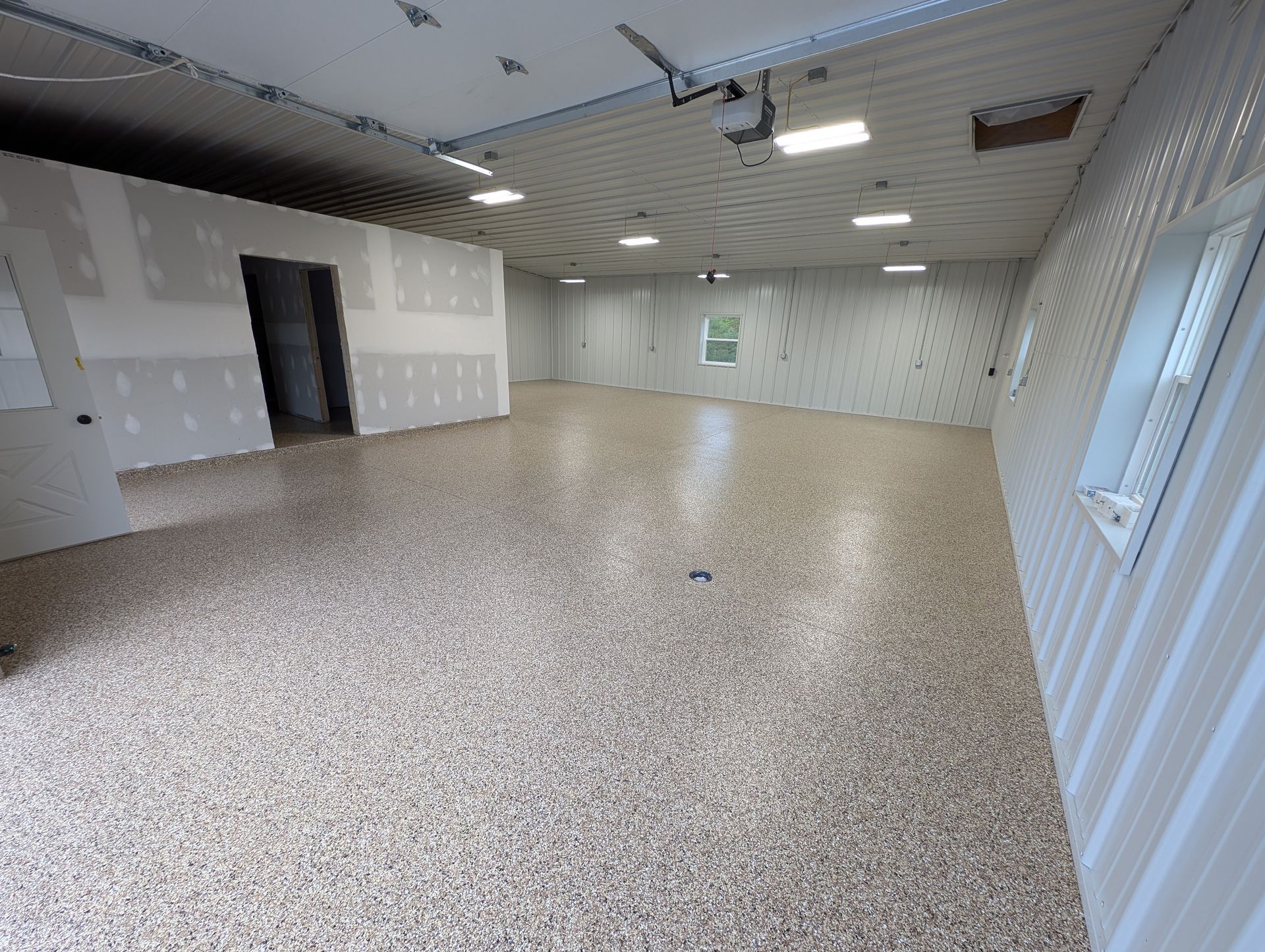 Empty office room with speckled floor, white walls, ceiling lights, and windows on the right.