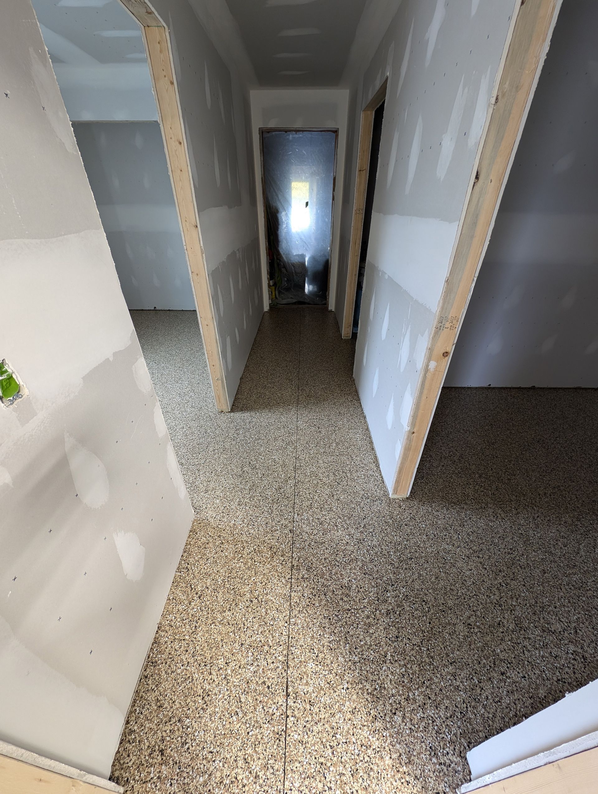 Narrow hallway in an unfinished house with beige walls, gray carpet, and doorways on both sides.