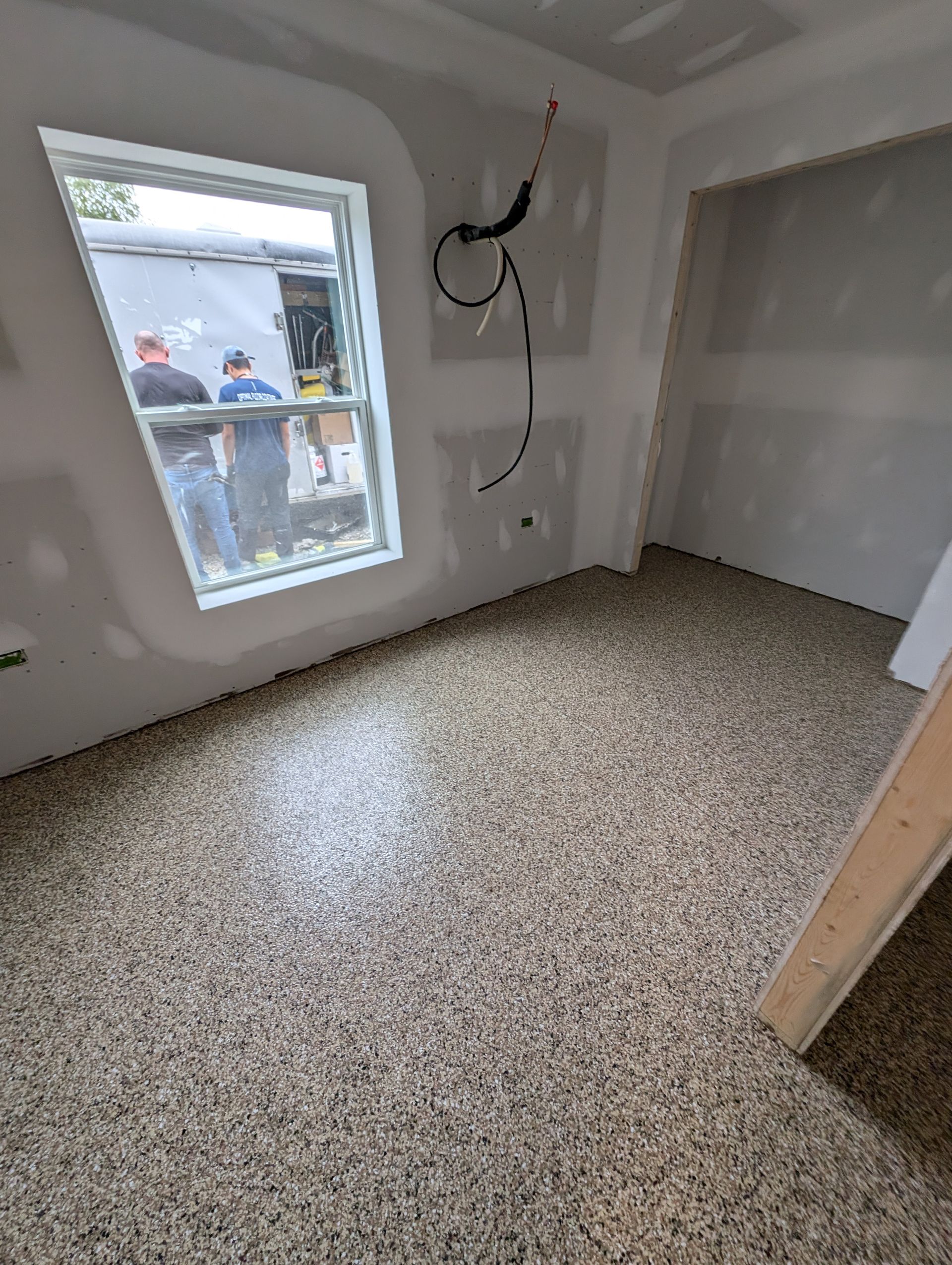 Empty unfinished room with terrazzo floor, white walls, a window, and exposed electrical wiring.