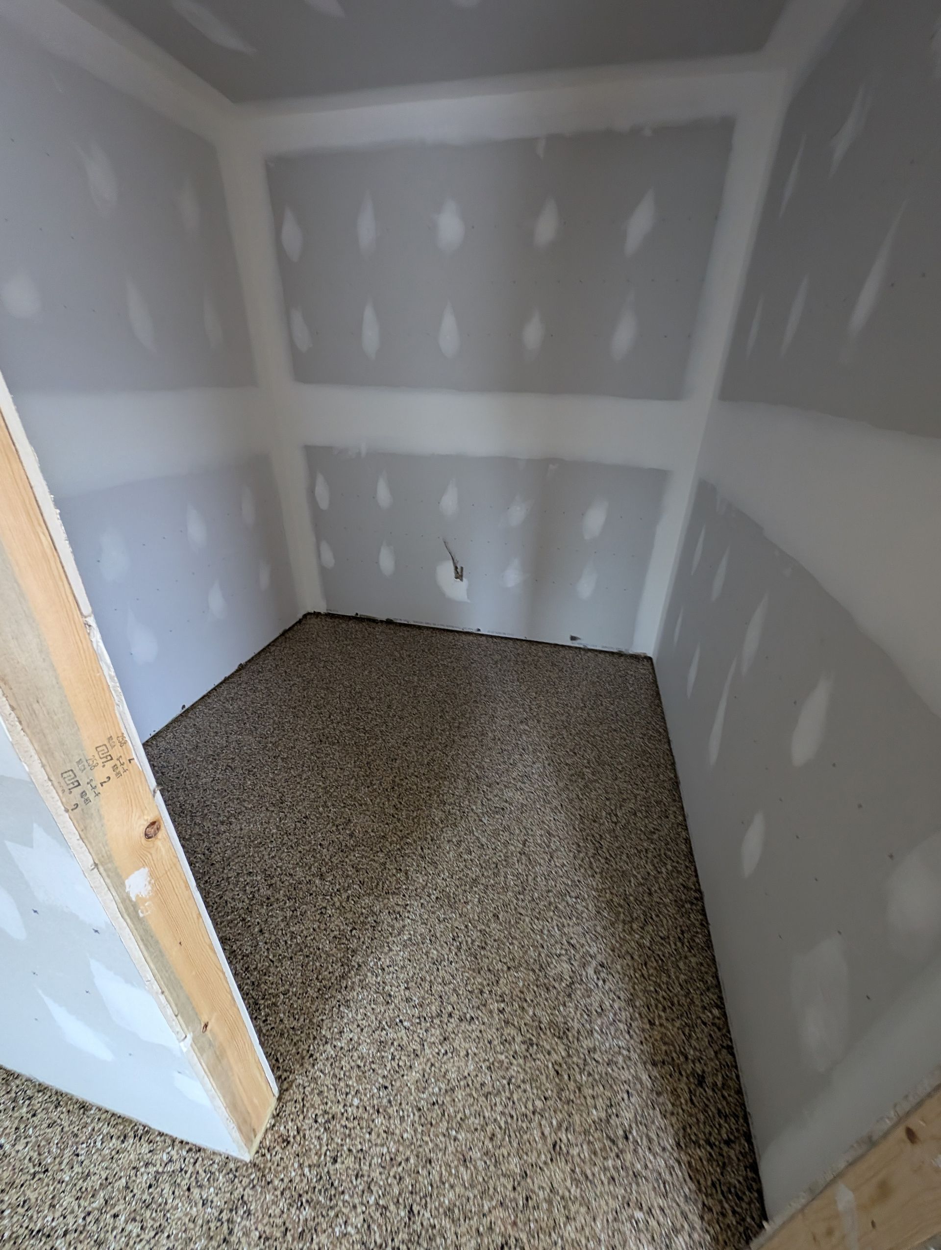 Empty unfinished closet with gray drywall and speckled carpet flooring.