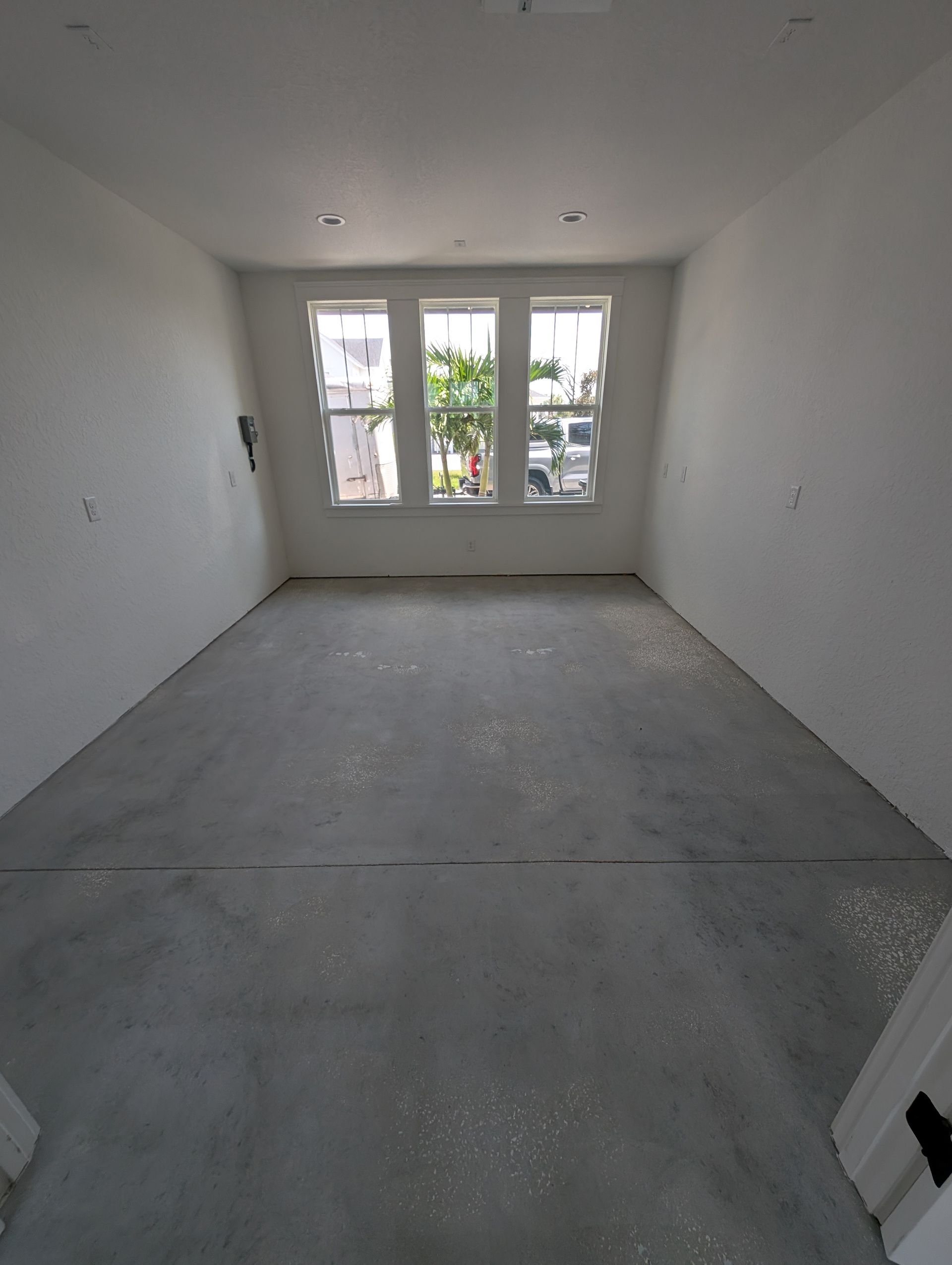 Empty white room with bare concrete floor and windows at the far end