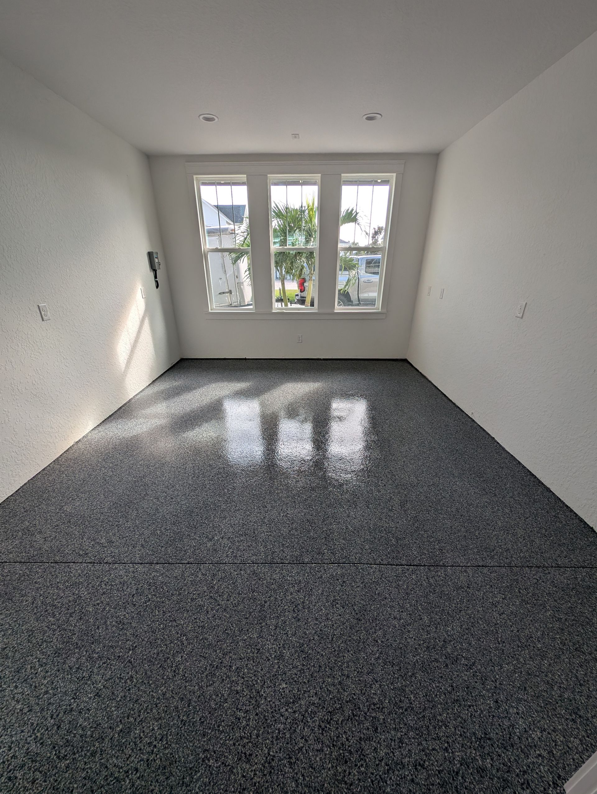 Empty white room with glossy speckled floor and double glass doors opening to greenery