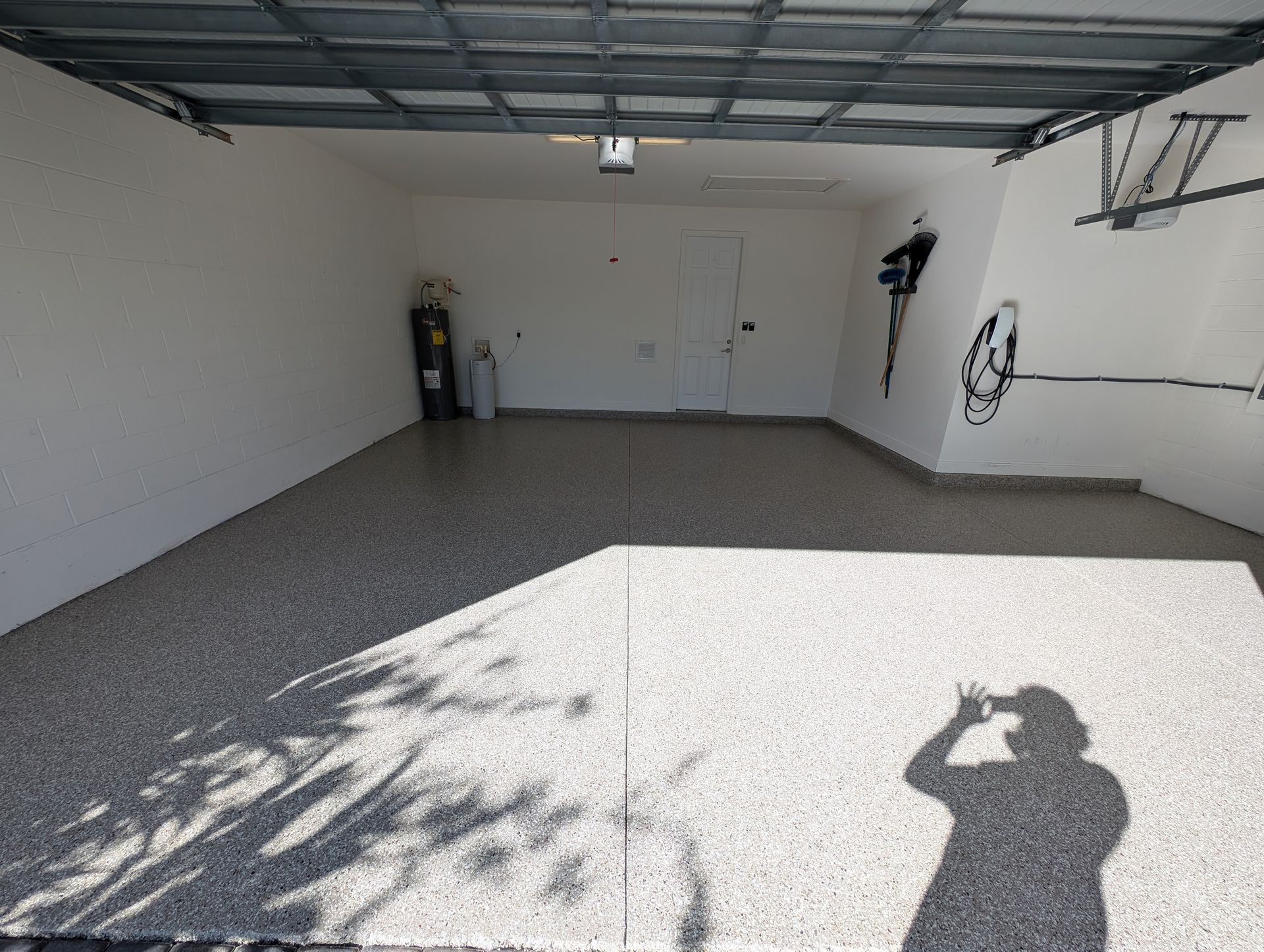 Empty two-car garage with open door, white walls, gray floor, and sunlight casting shadows inside.