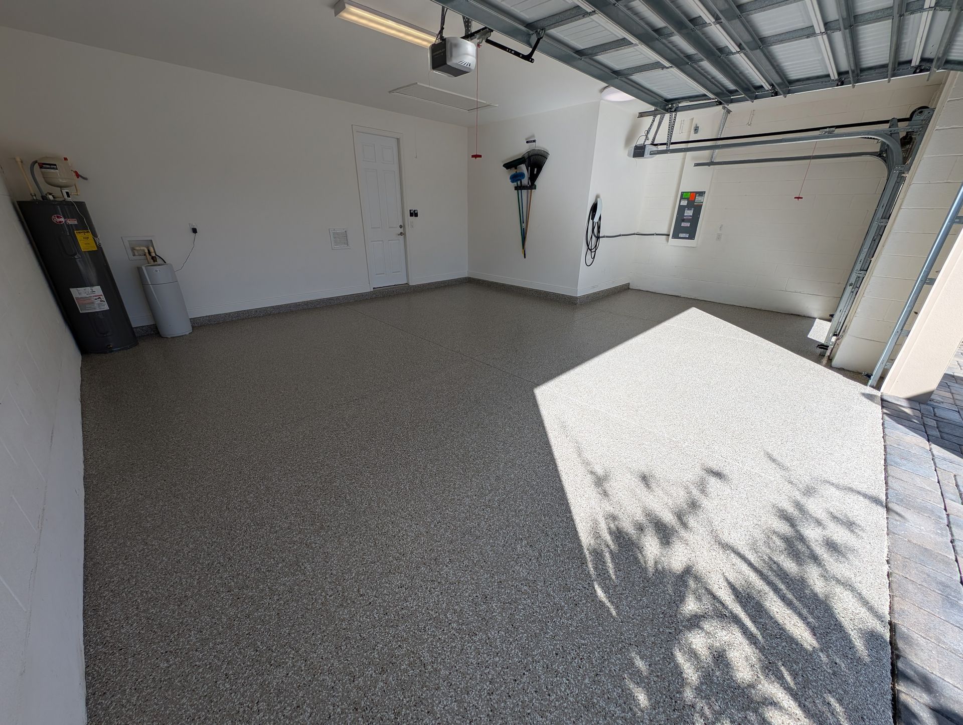 Empty garage with speckled gray floor, white walls, and sunlight spilling in from the open door