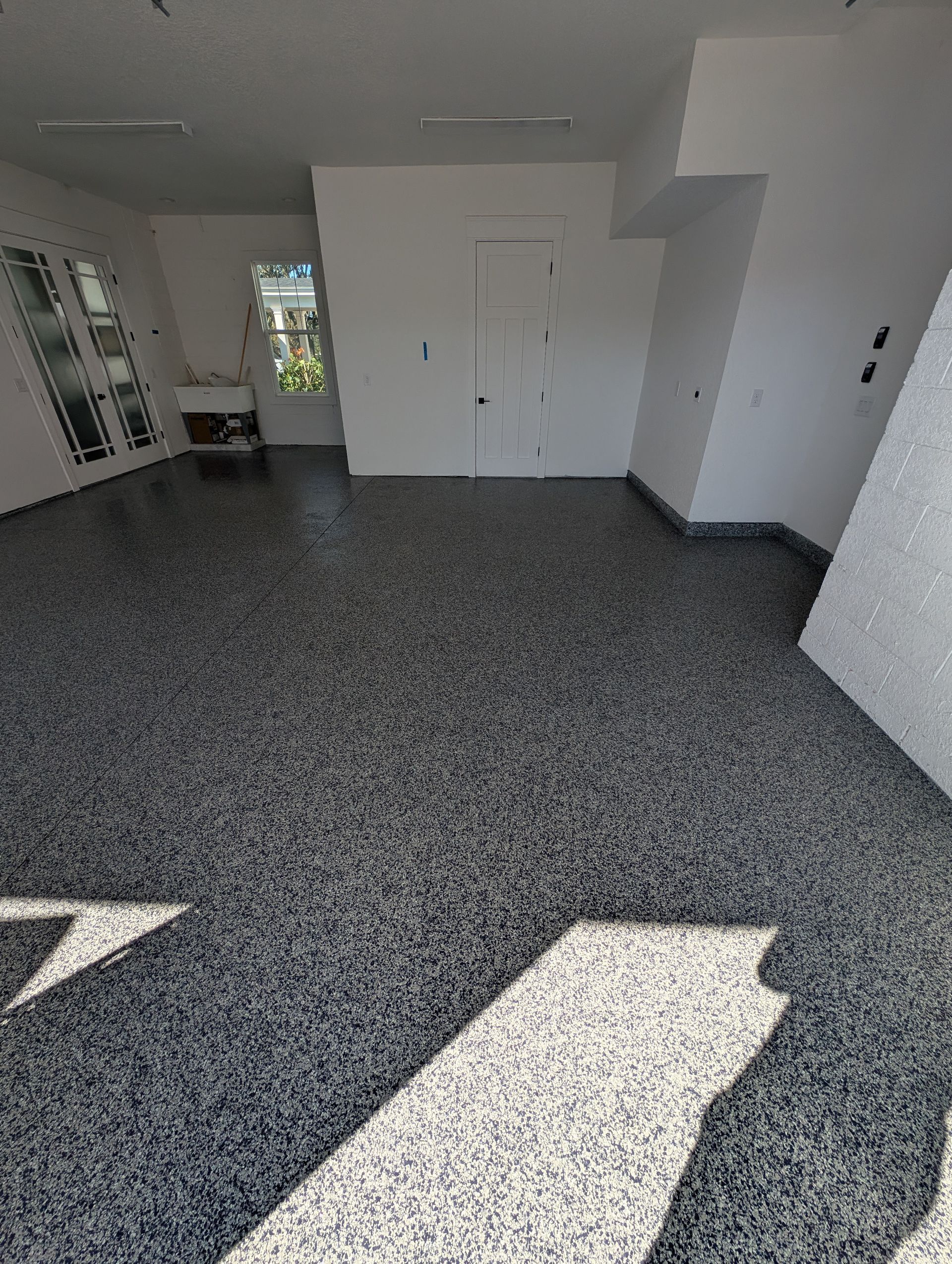 Empty room with speckled floor, white walls, and sunlight from a doorway and windows.