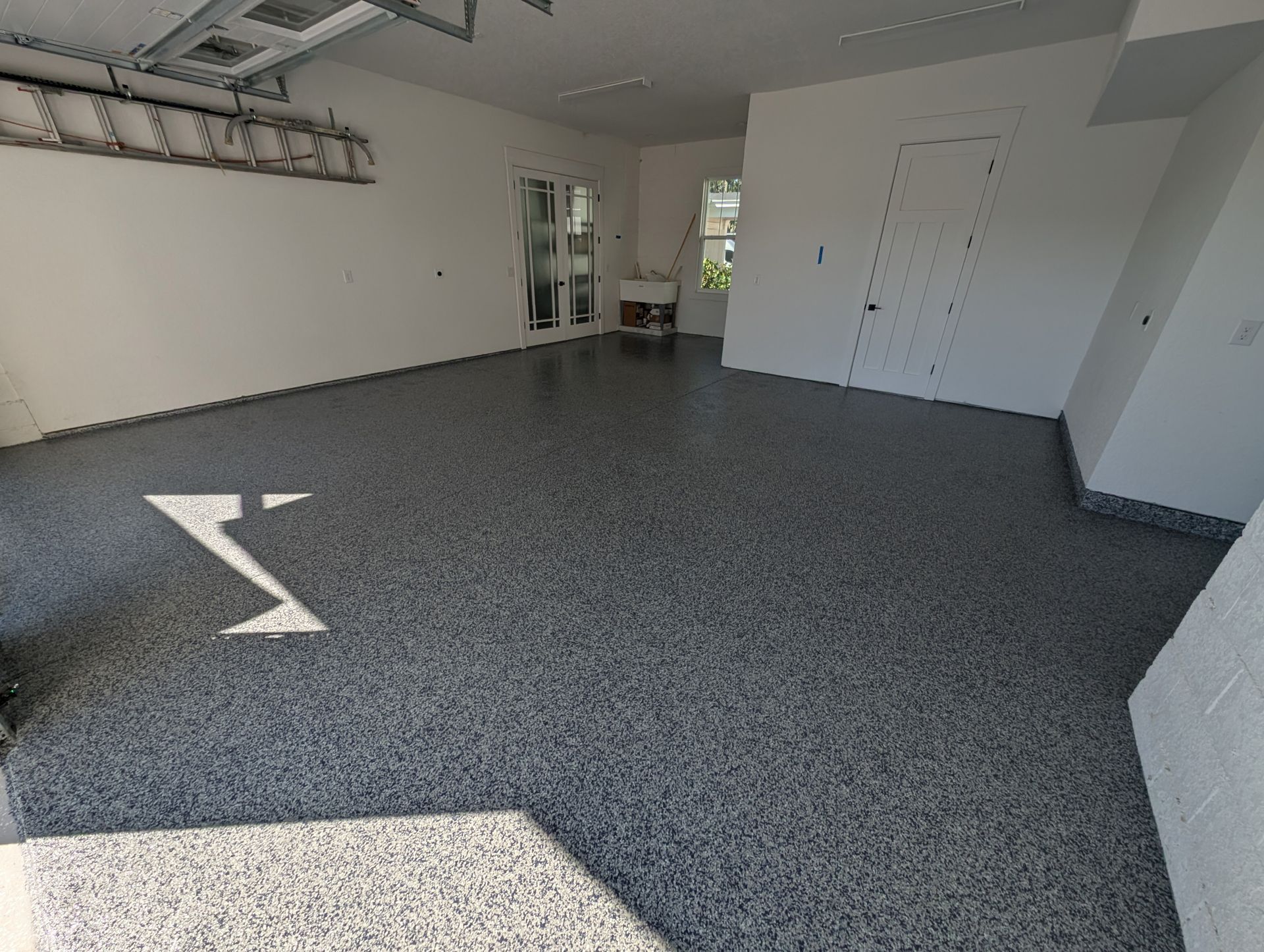 Empty garage with speckled floor, white walls, and sunlight streaming in from the left.