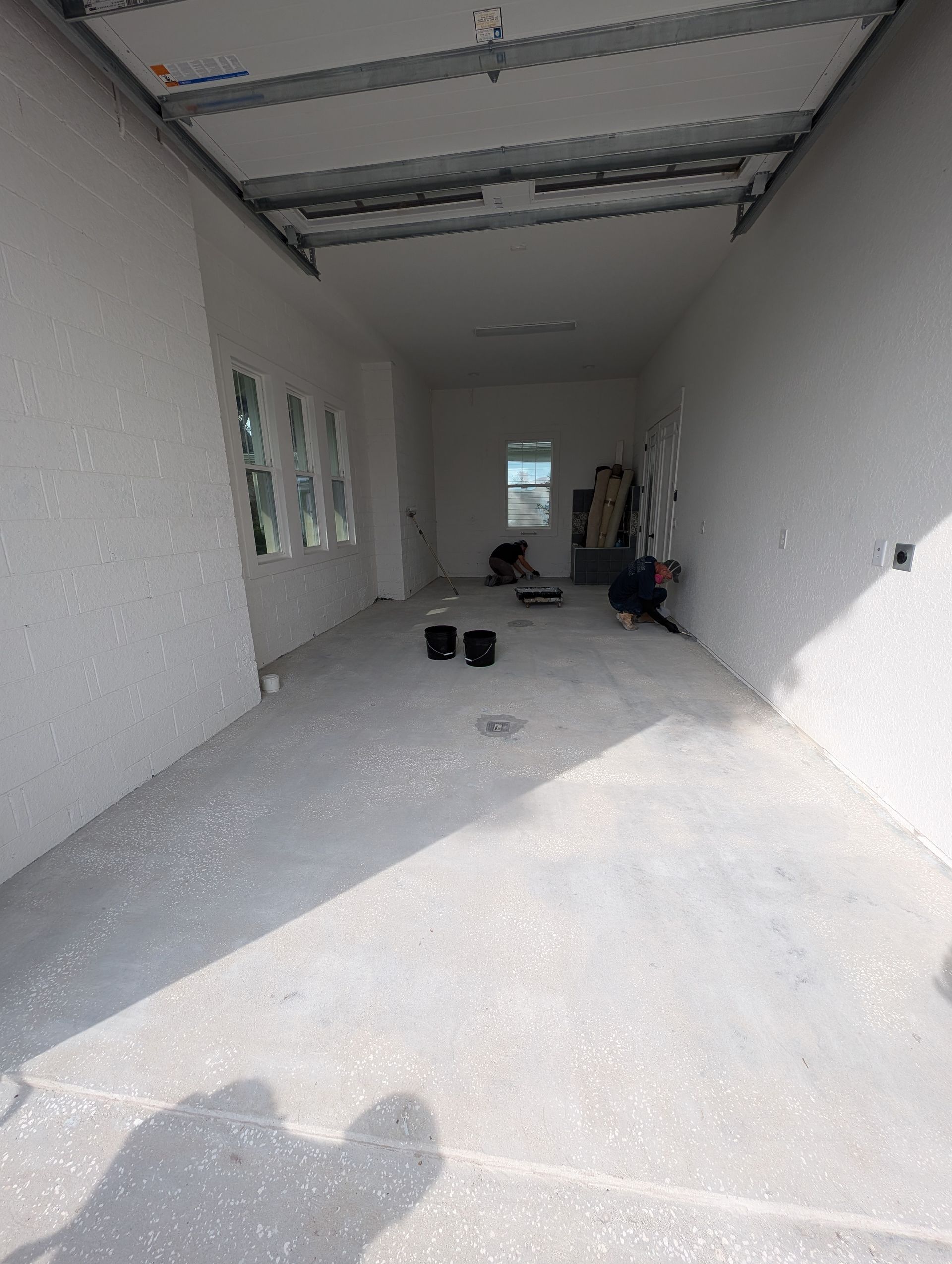 Long, unfinished room under construction with white walls, exposed ceiling, and scattered tools on the floor