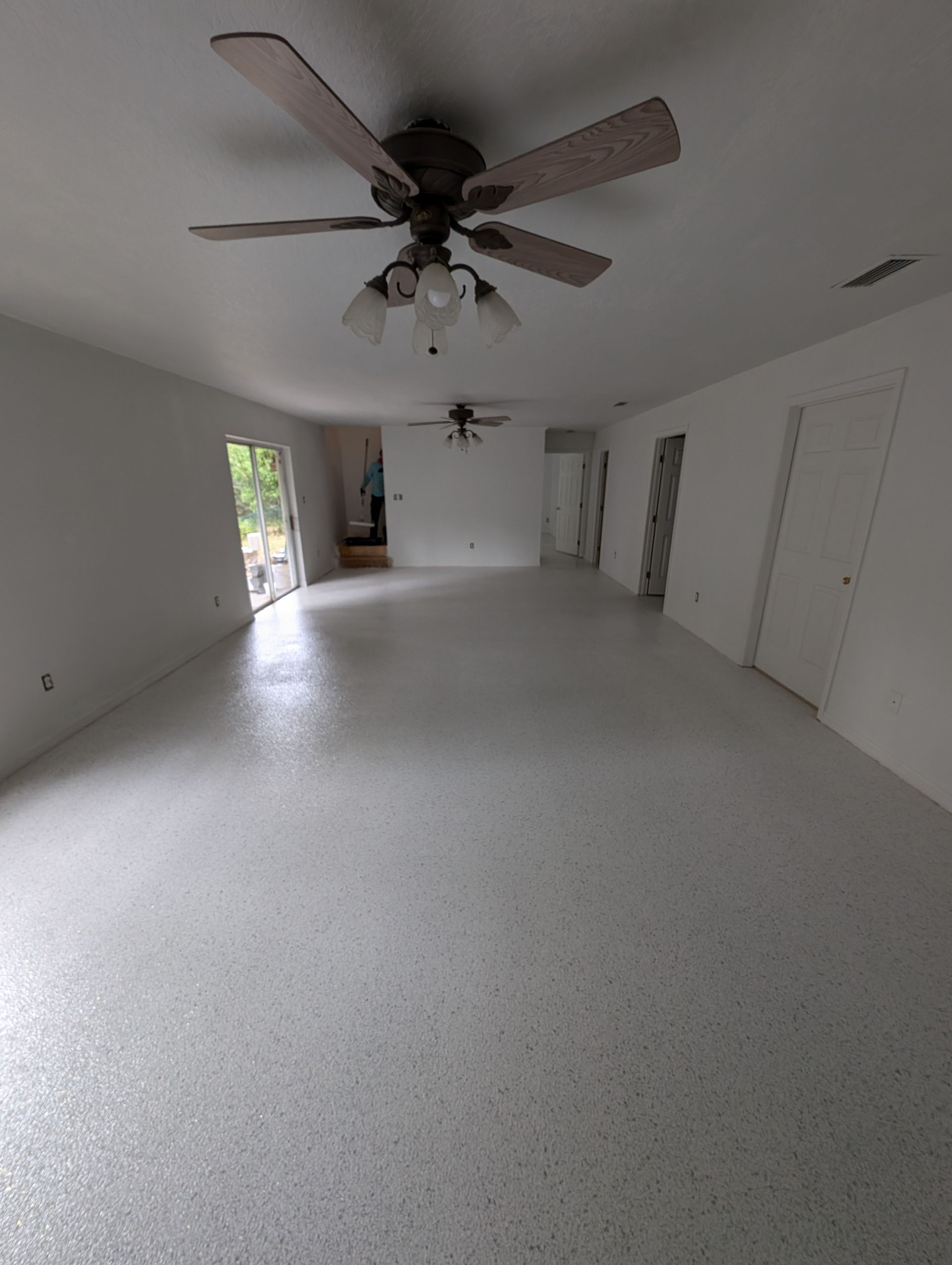 Empty white living room with ceiling fan, glossy floor, and doorways along the walls.