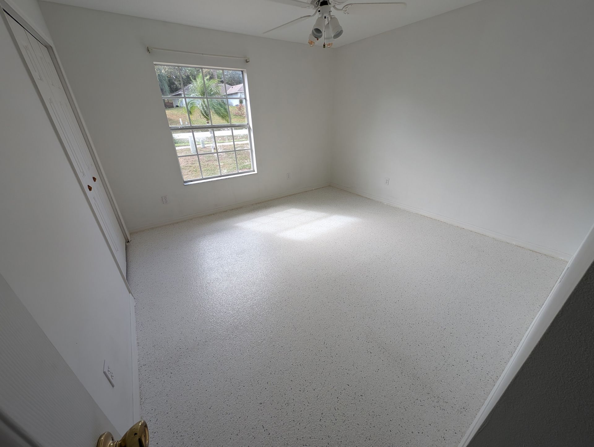 Empty white bedroom with speckled floor and a window letting in daylight