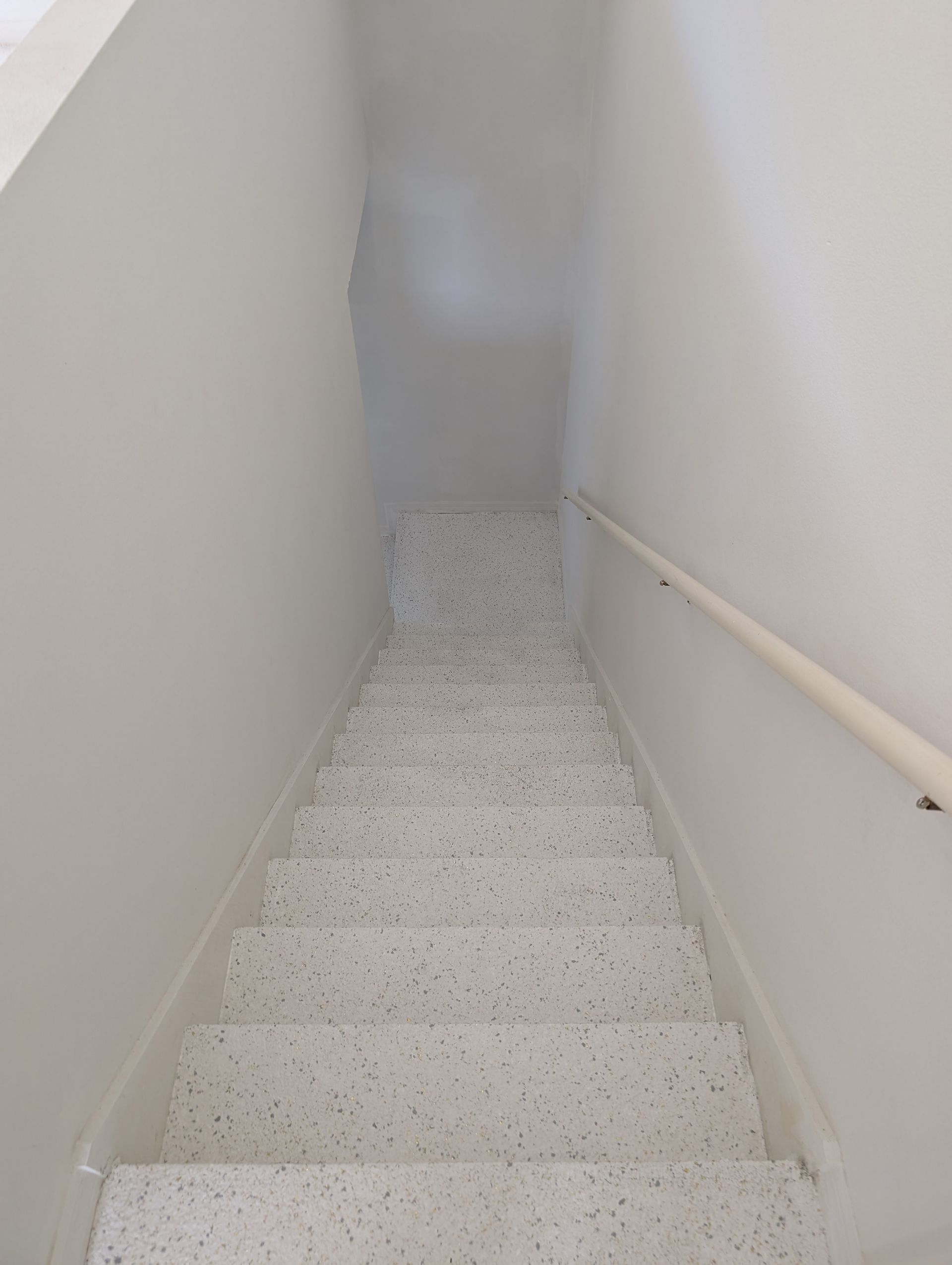 Narrow white stairwell with speckled steps and a handrail along the right wall