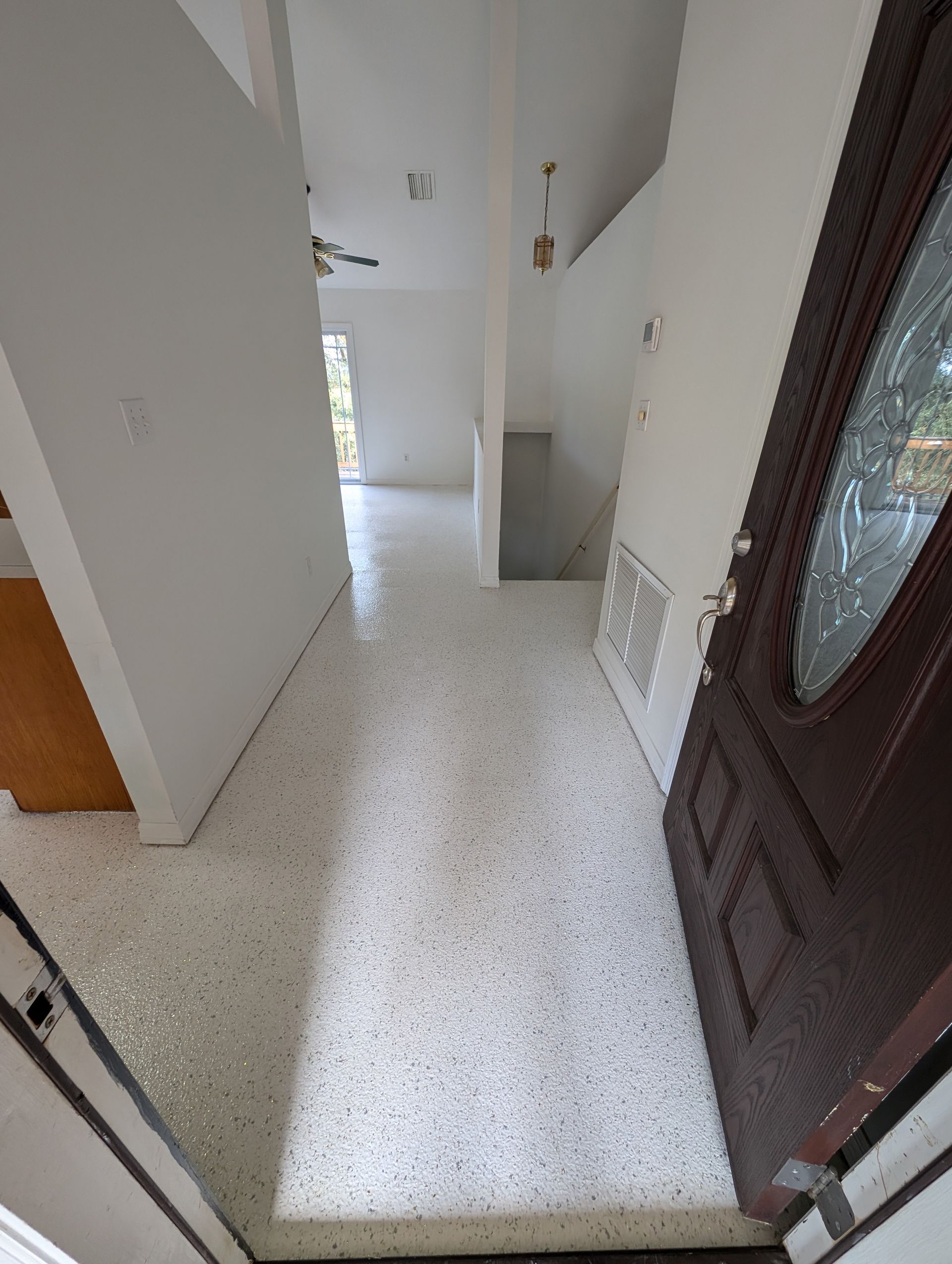 Narrow white hallway with speckled floor, open doorway, and dark front door on the right.