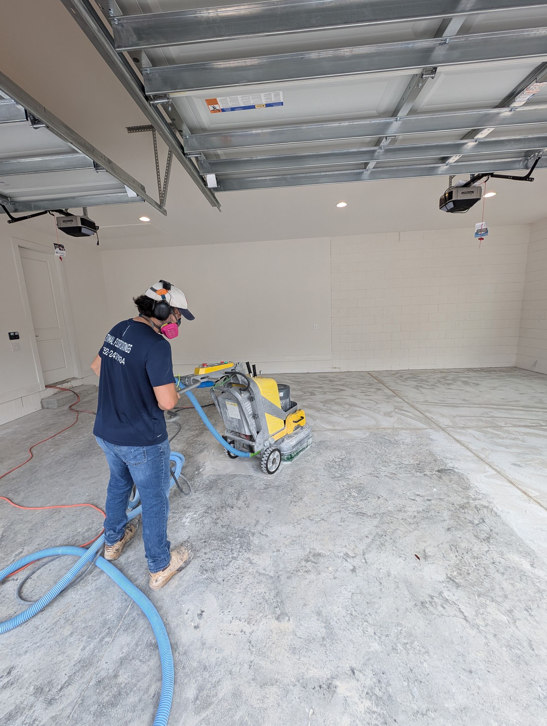 Worker operating floor grinder in a bare garage under a metal ceiling frame