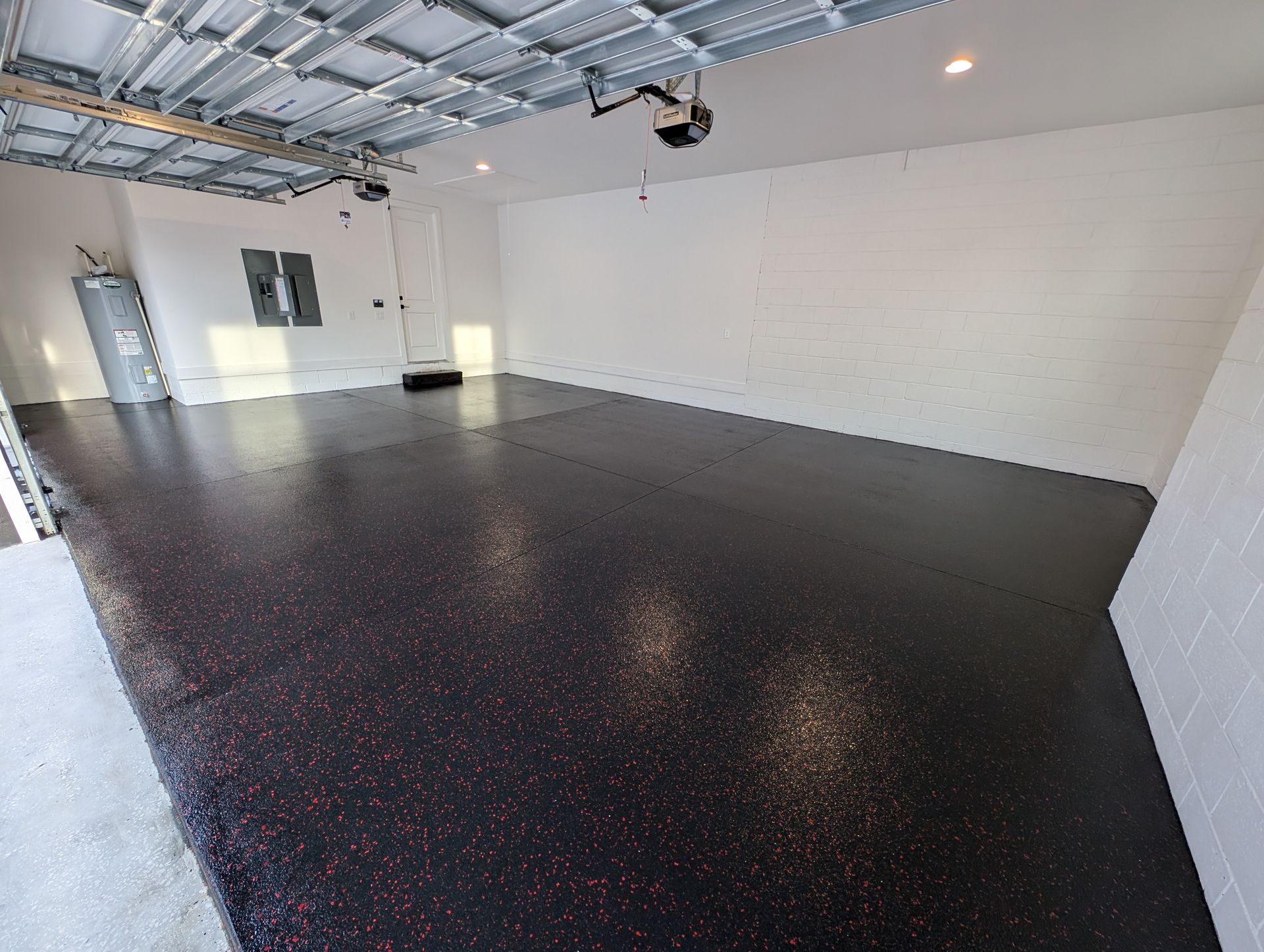 Empty garage with a black epoxy floor, white walls, and exposed ceiling beams and lights.