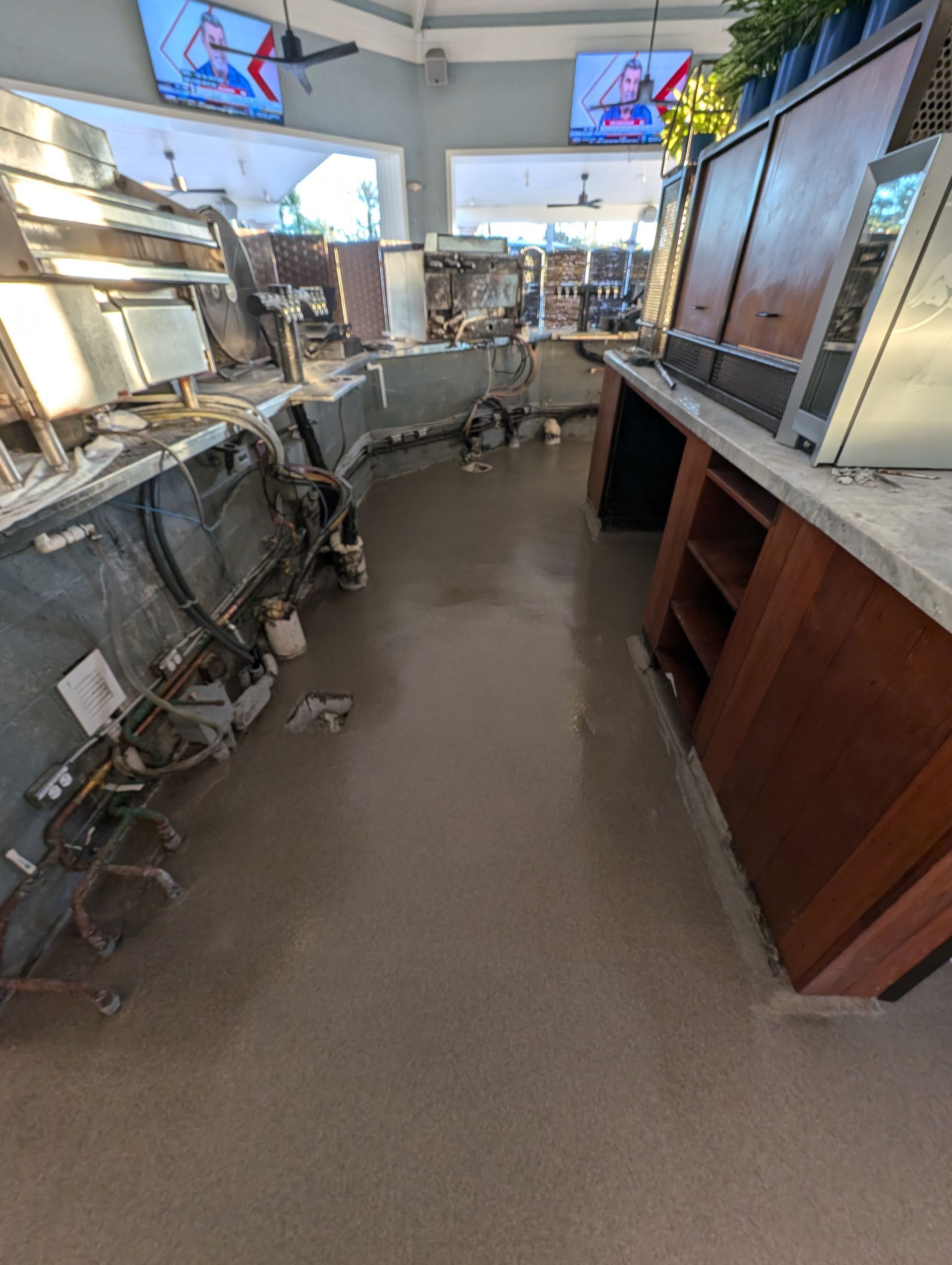 Empty restaurant counter area with stainless prep tables, shelves, and two TVs above a narrow aisle