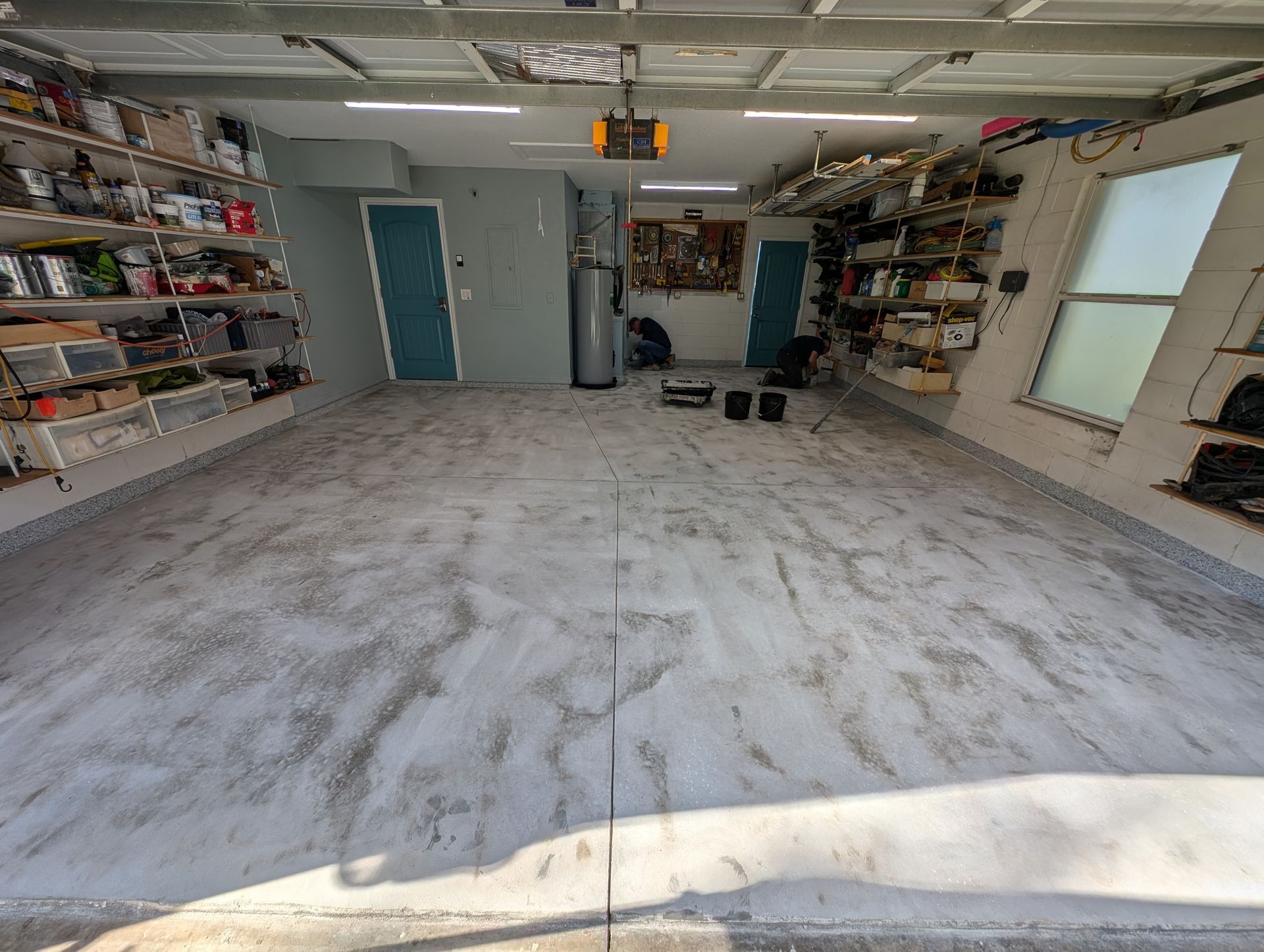 Spacious garage interior with shelves, tools, a blue door, and a small ladder under bright overhead lights