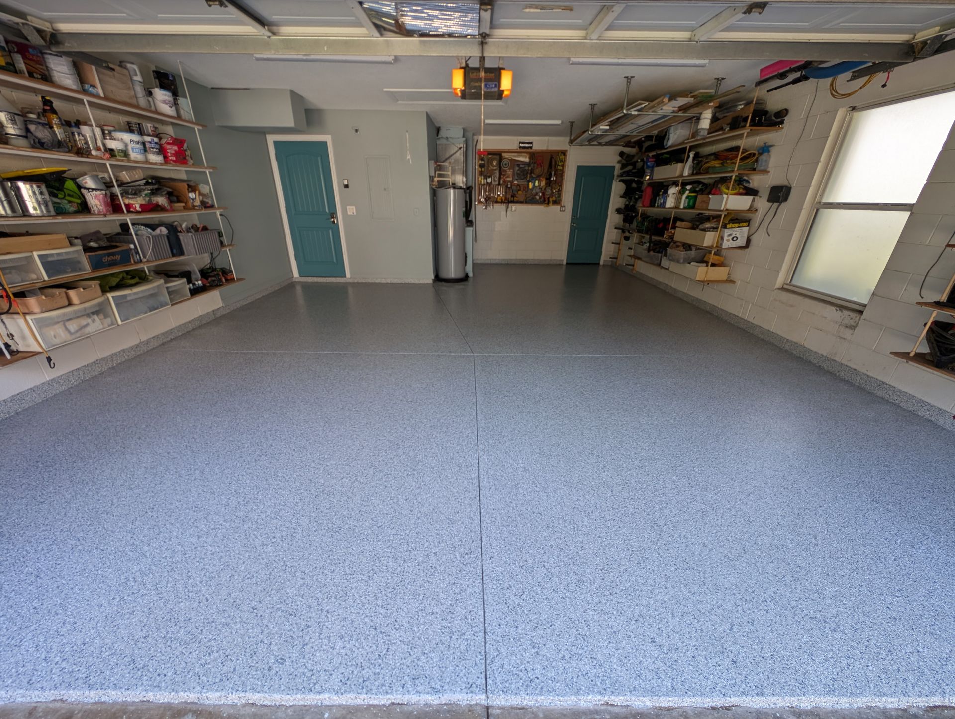 Interior of a garage with gray speckled floor, shelves on both sides, and two doors at the back.
