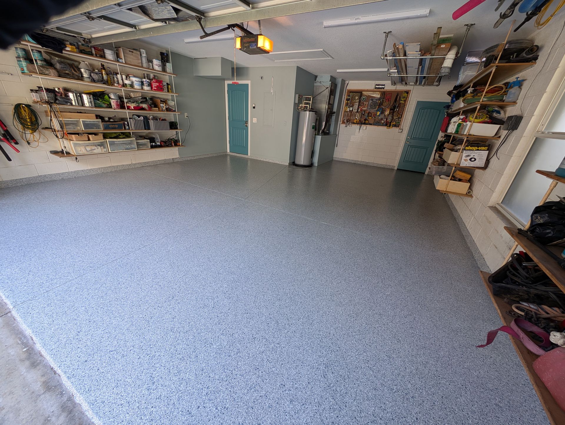 Spacious garage with shelves of gear, a speckled floor, and two teal doors at the back.
