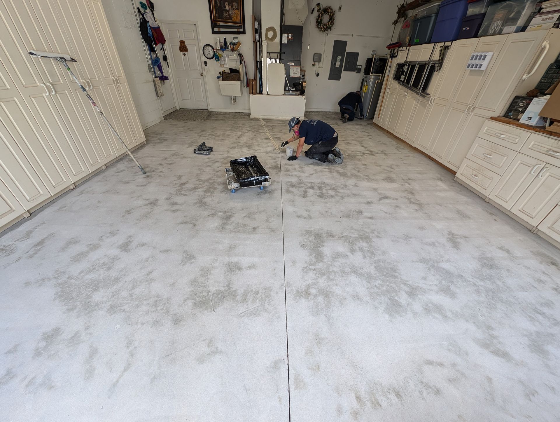 Garage interior with white cabinets and a concrete floor, two people kneeling near tools in the center.