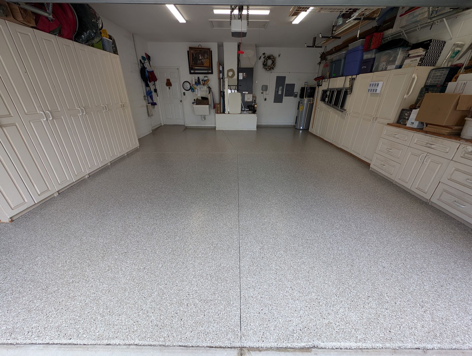 Garage workshop with white cabinets, speckled floor, and tools along the walls