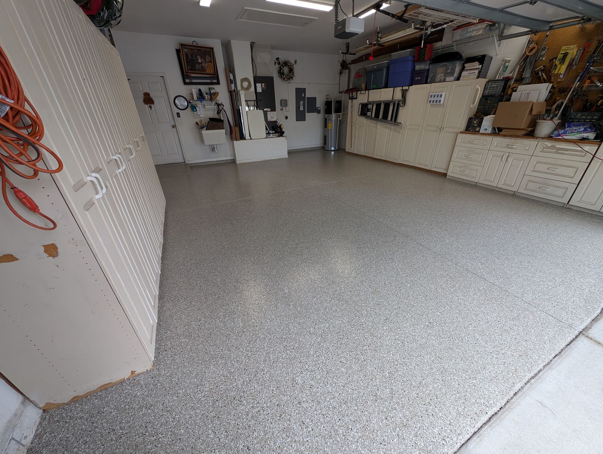 Cluttered garage with gray speckled floor, white cabinets, tools, and storage shelves along the walls