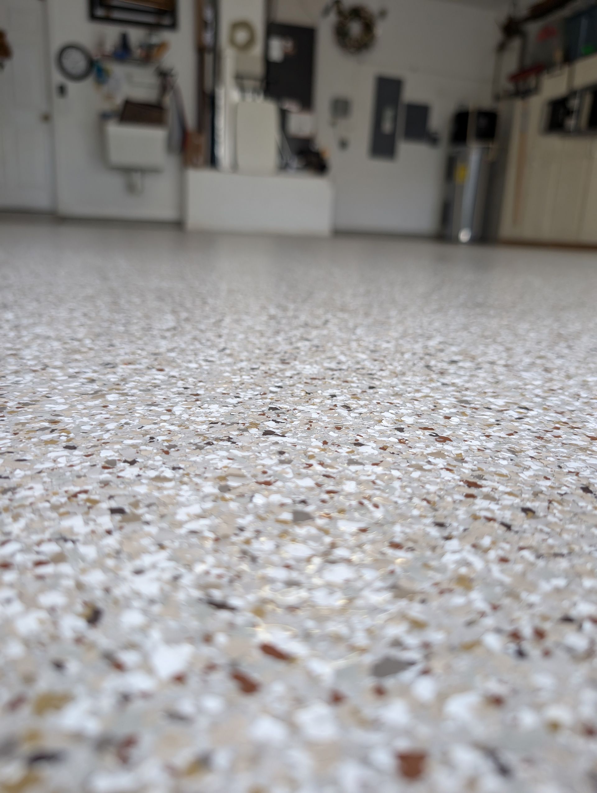 Low-angle view of a speckled epoxy floor in a garage or workshop, with tools and cabinets blurred in the background.