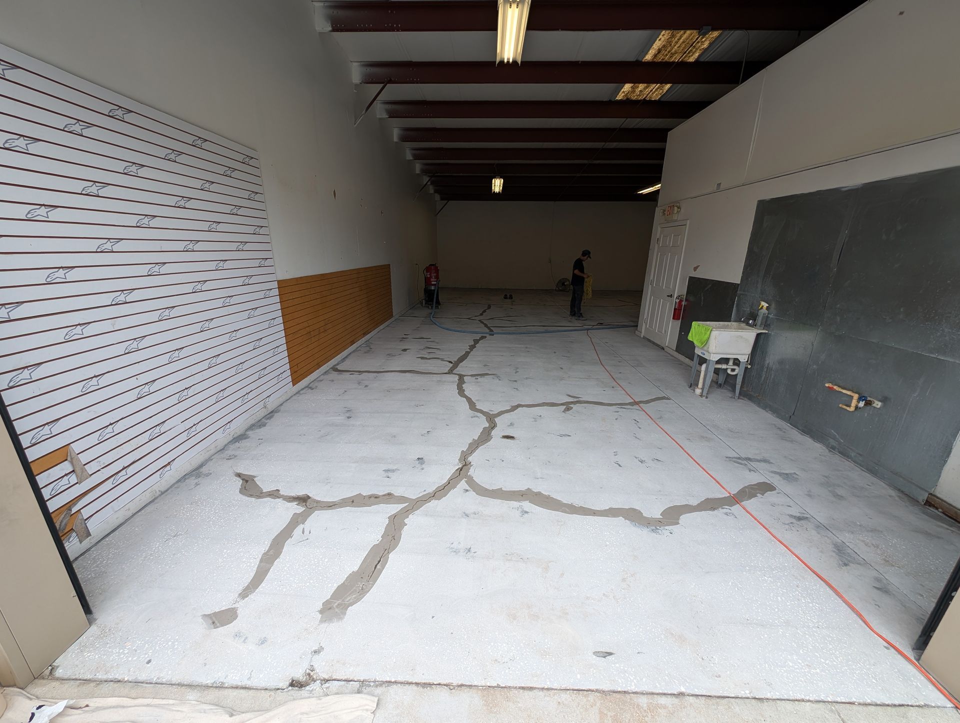 Empty unfinished garage with cracked concrete floor, exposed beams, and tools against the walls