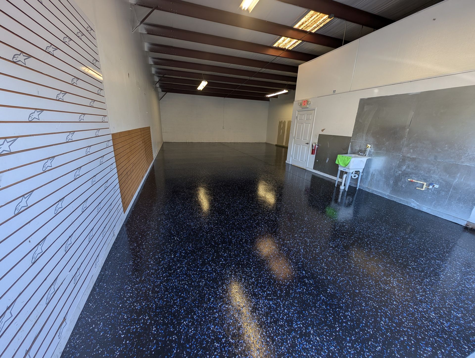 Empty warehouse with glossy black floor, white walls, and a small worktable near the back.