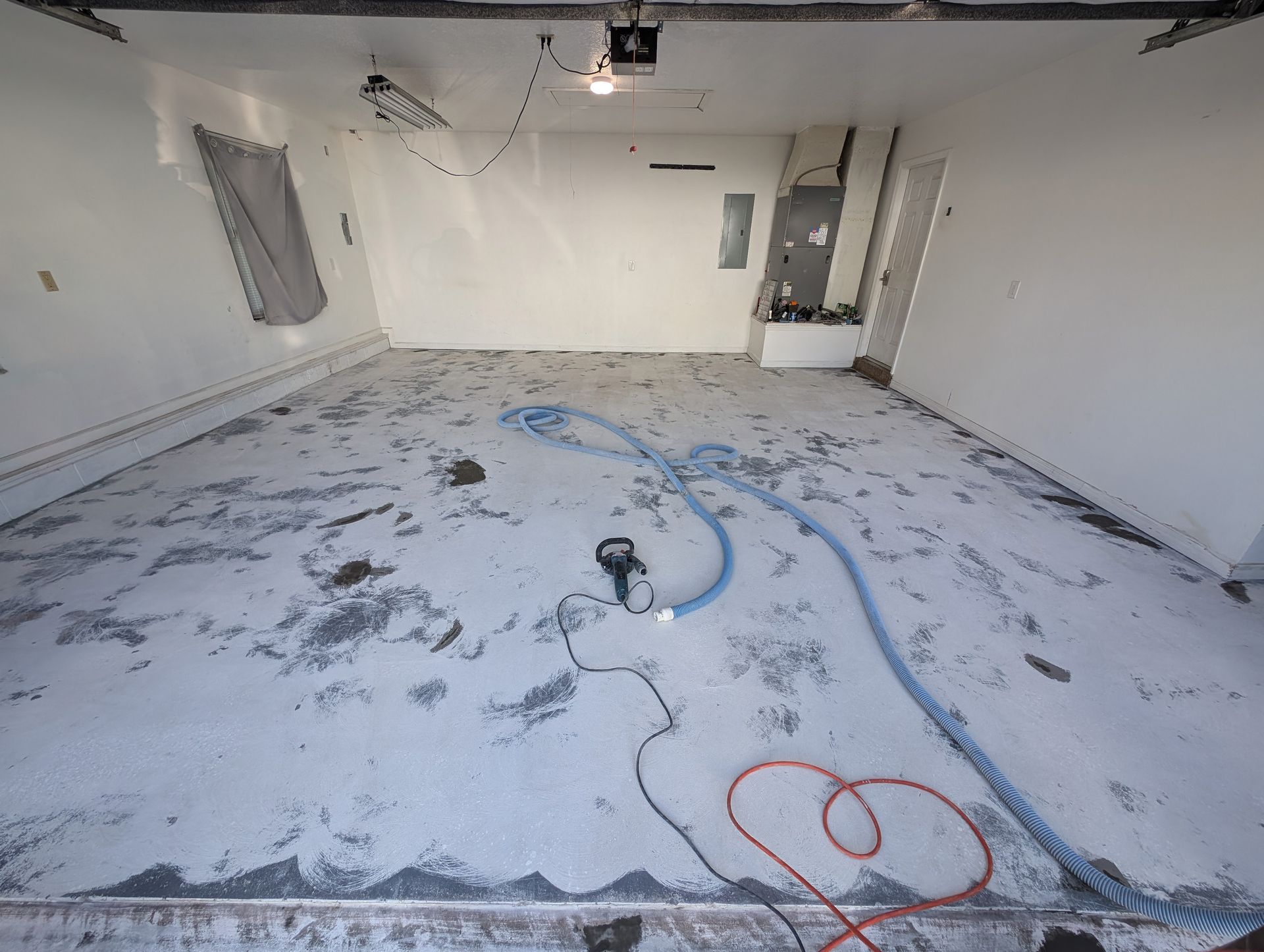 Empty white room with paint-splattered floor, scattered cords, and a small tool near the center.