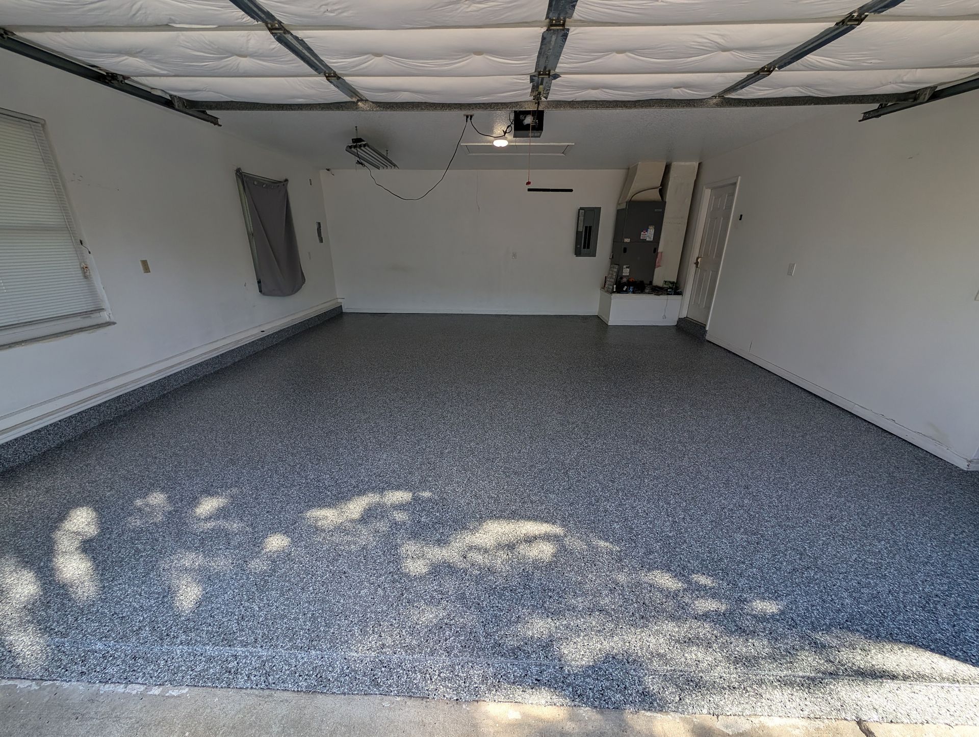 Empty garage with speckled epoxy floor, white walls, windows, and an open doorway.
