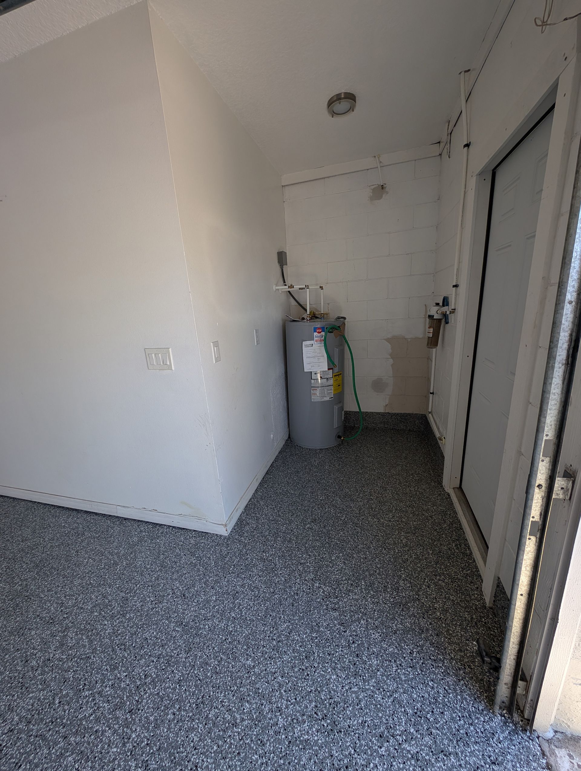 Empty white utility room with speckled gray floor and a water heater near the back wall.