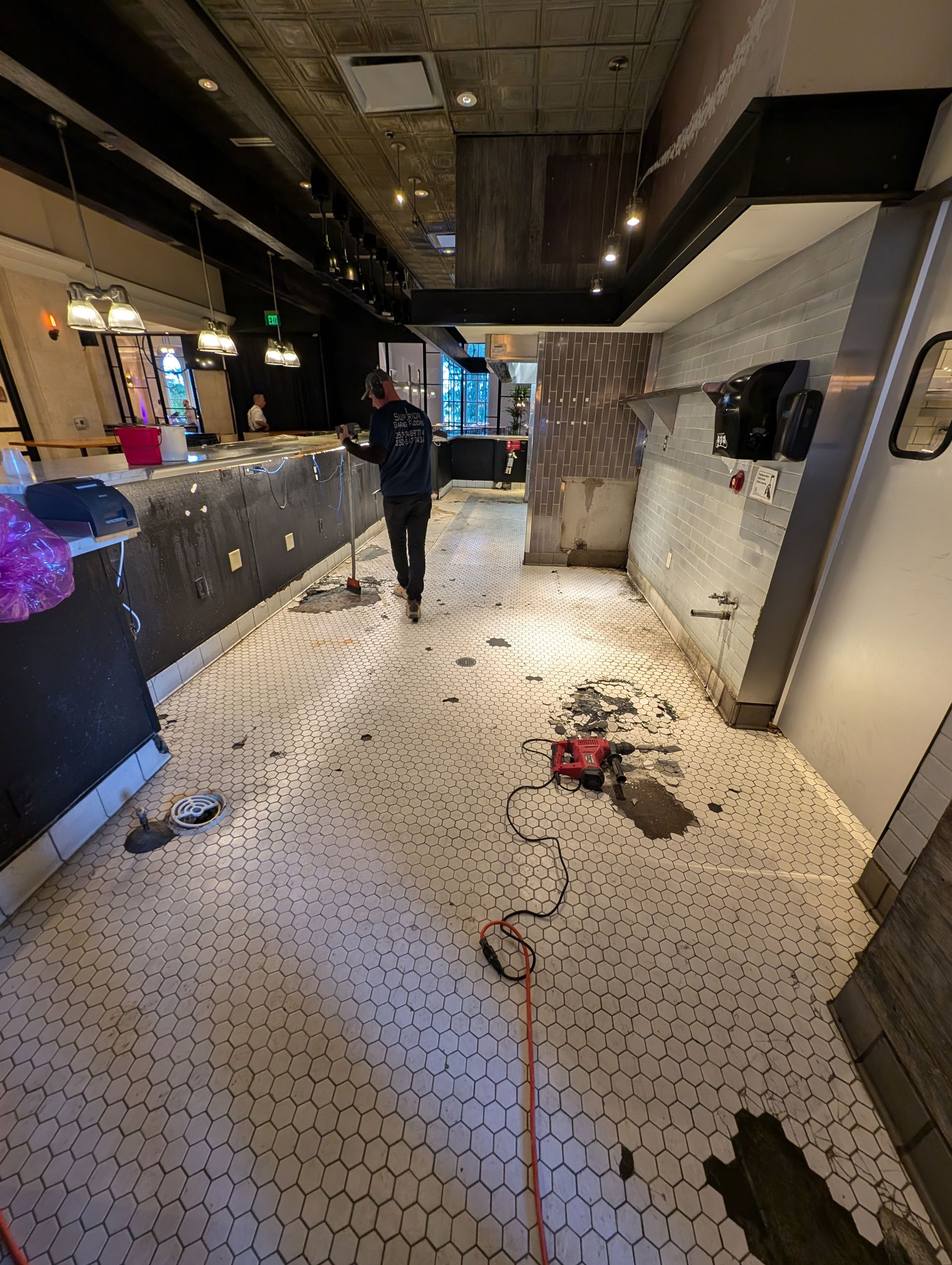 Damaged indoor walkway with debris and scattered ceiling tiles; a person walks away in the background.