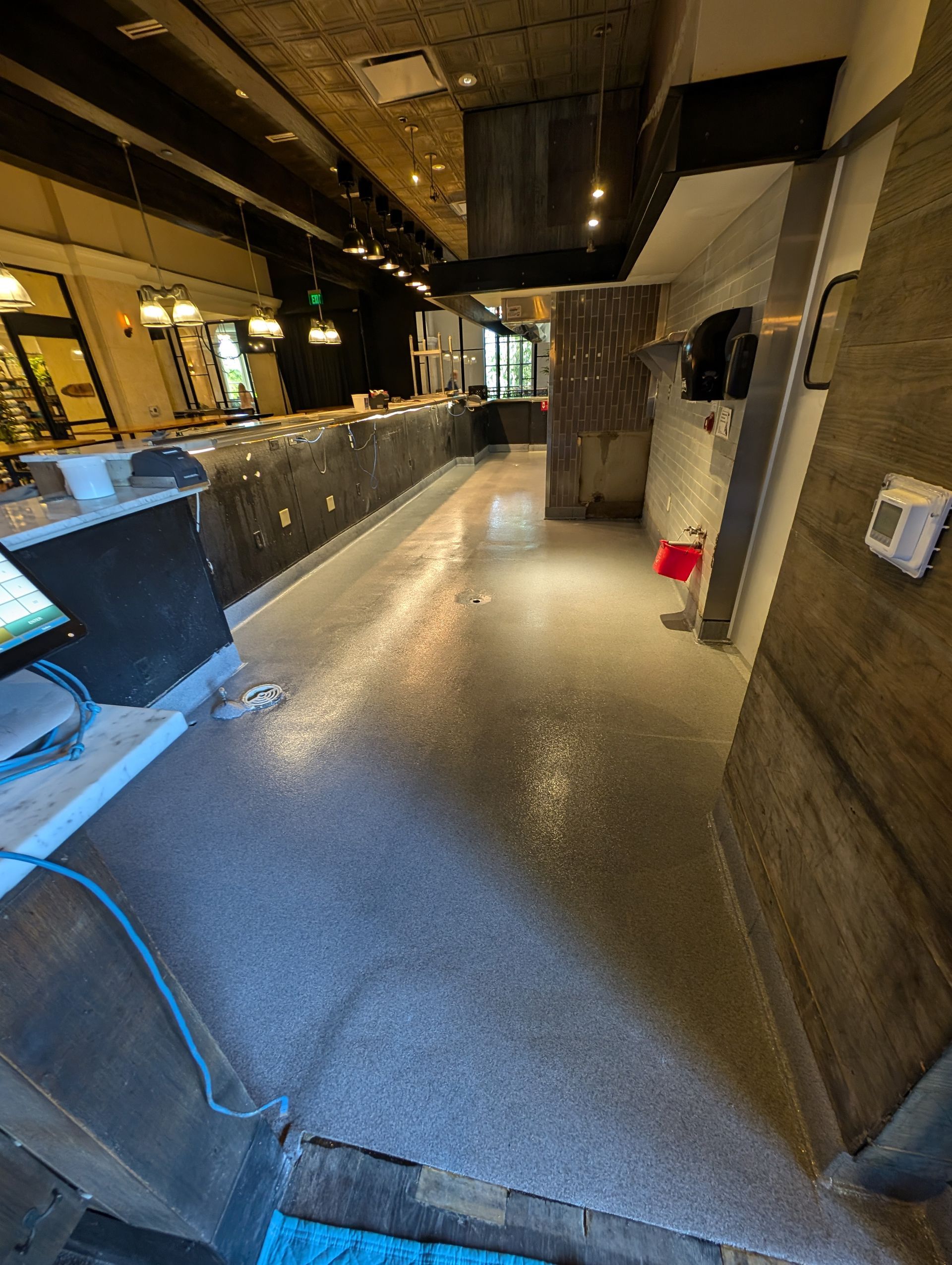 Empty indoor corridor with metal railings, gray floor, and a red bucket near the wall