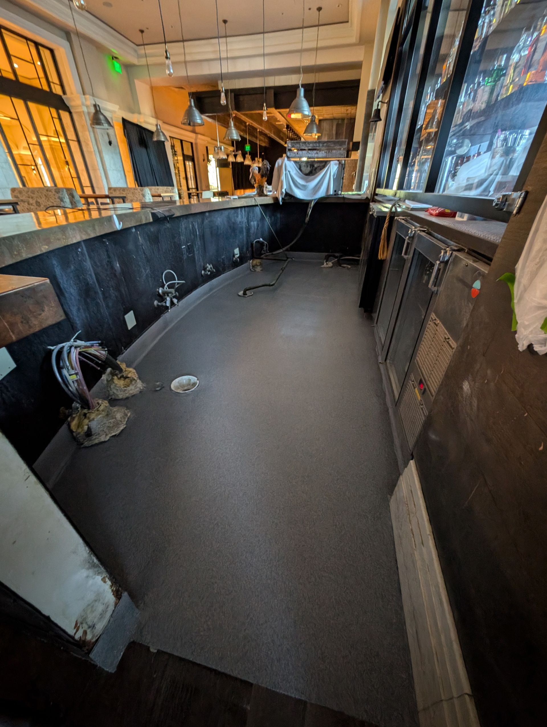 Empty bar interior with black counters, carpeted floor, and windows covered in plastic sheeting
