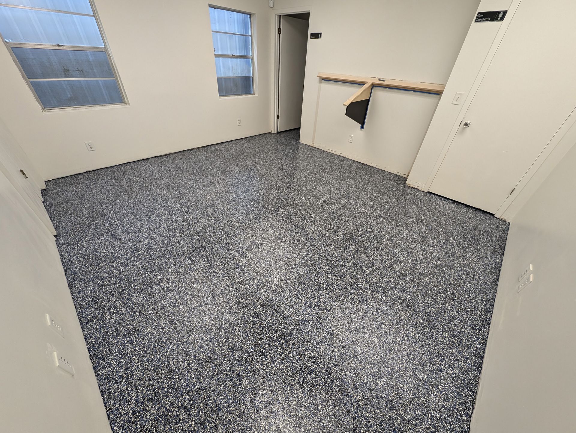 Empty room with speckled gray floor, white walls, blue windows, and a doorway to a utility area