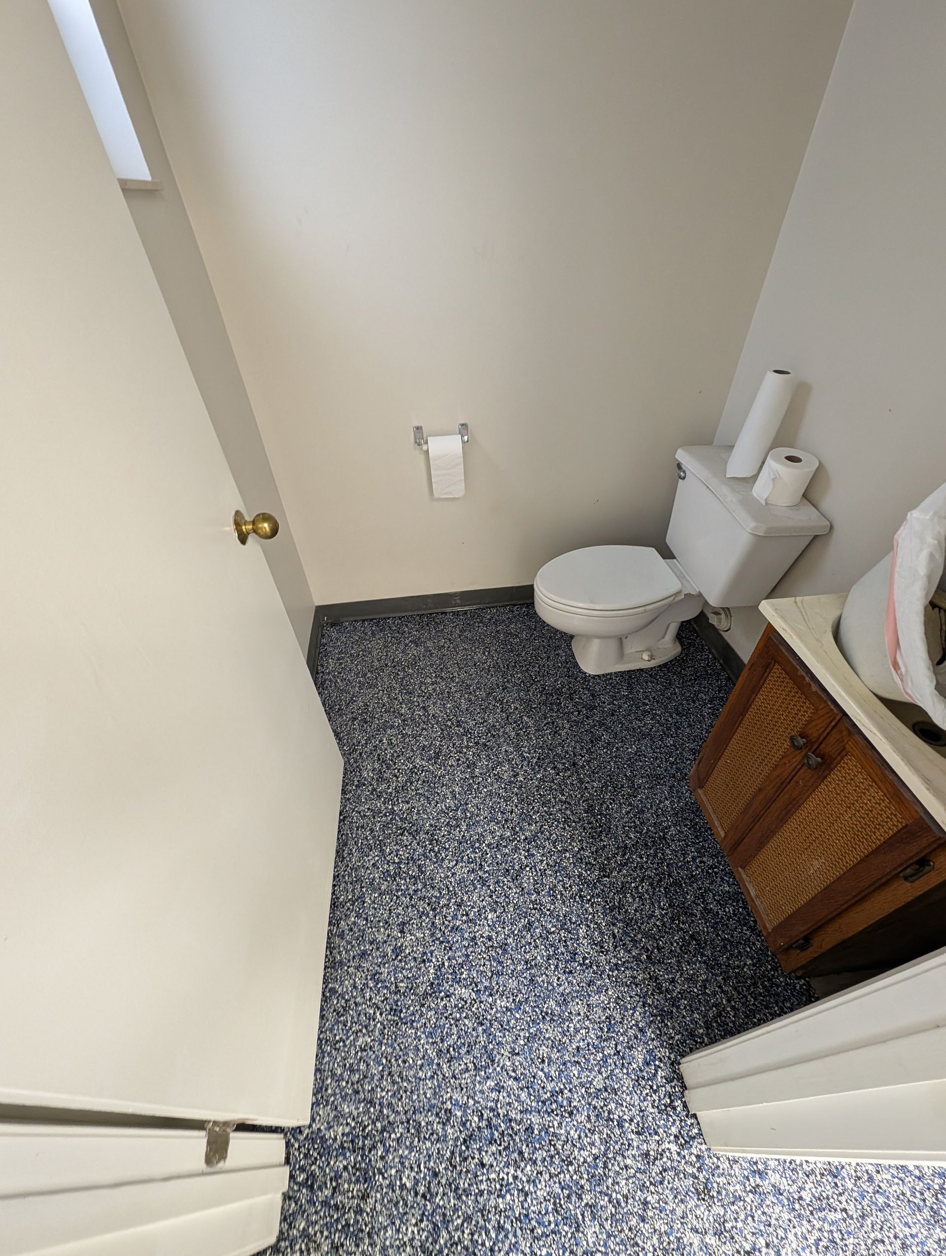 Small bathroom with a toilet, speckled floor, and vanity beside an open door.