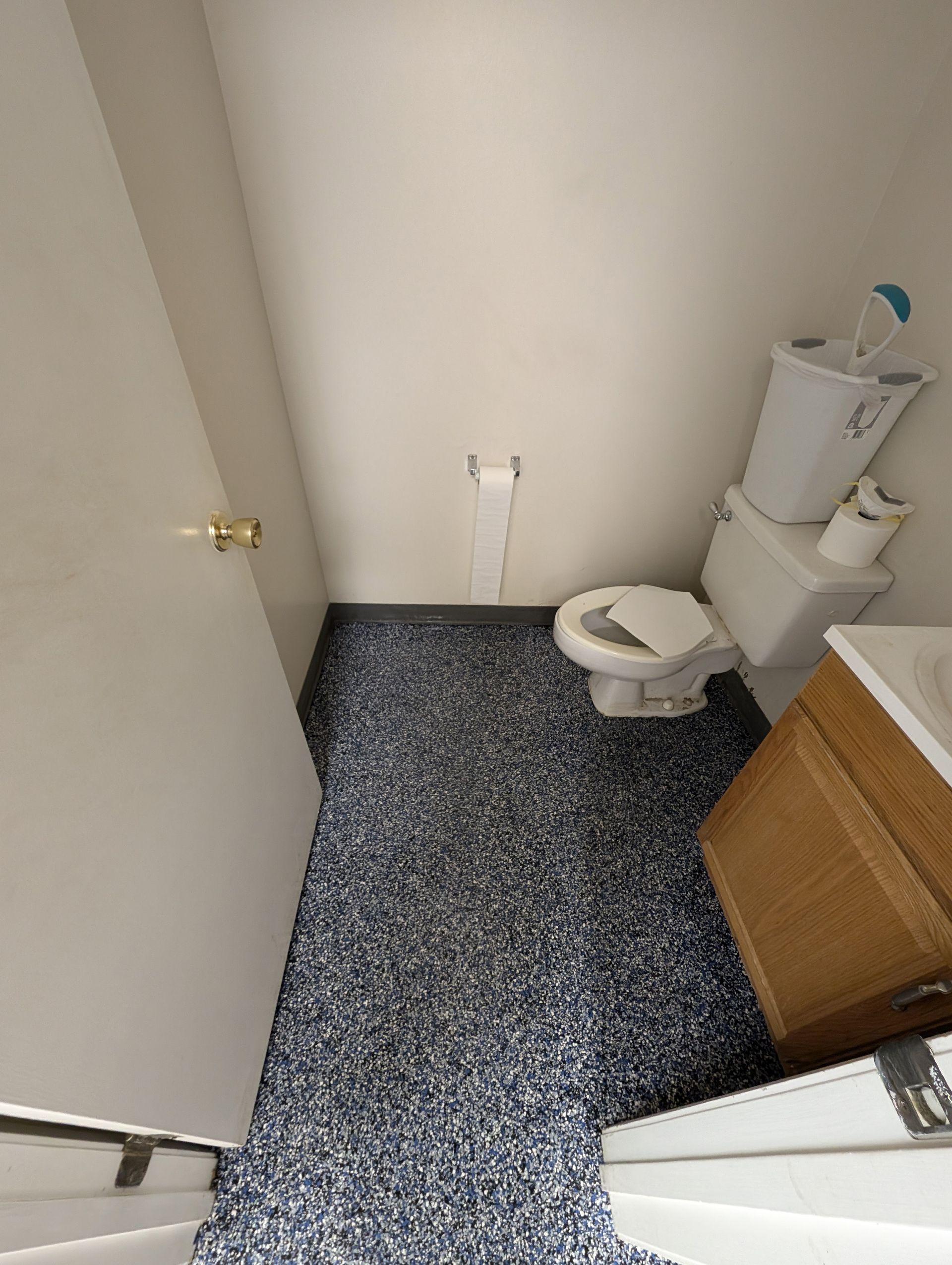 Small bathroom with toilet, vanity, and speckled dark floor in a tight space
