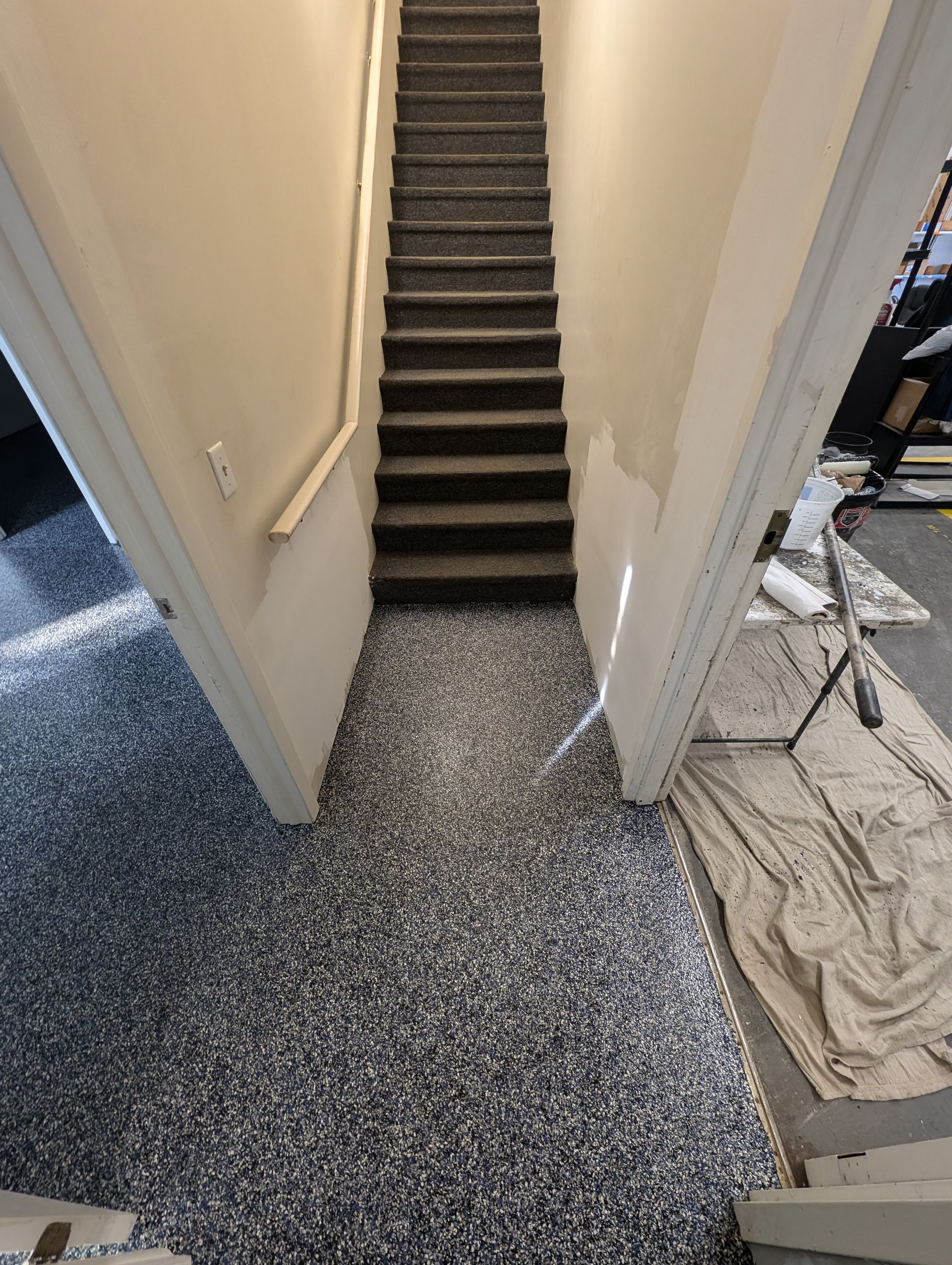 Narrow hallway with carpeted stairs and speckled flooring leading up to a landing.