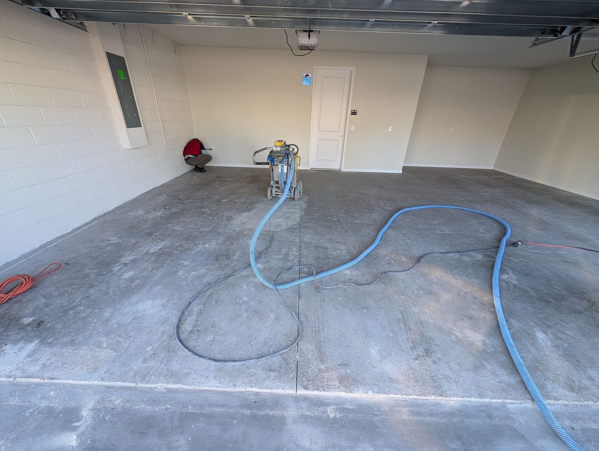 Empty garage with a floor grinder and blue hose on the concrete floor
