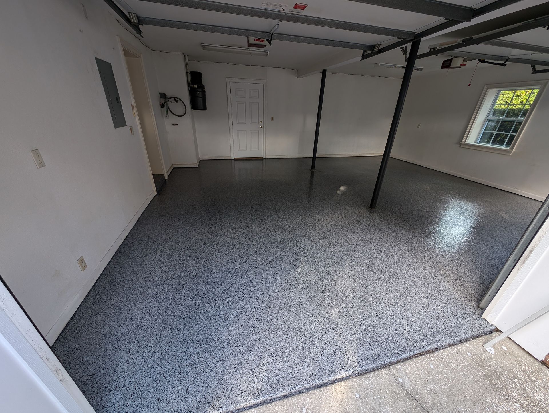 Empty garage with speckled gray floor, white walls, ceiling tracks, and a window on the right.