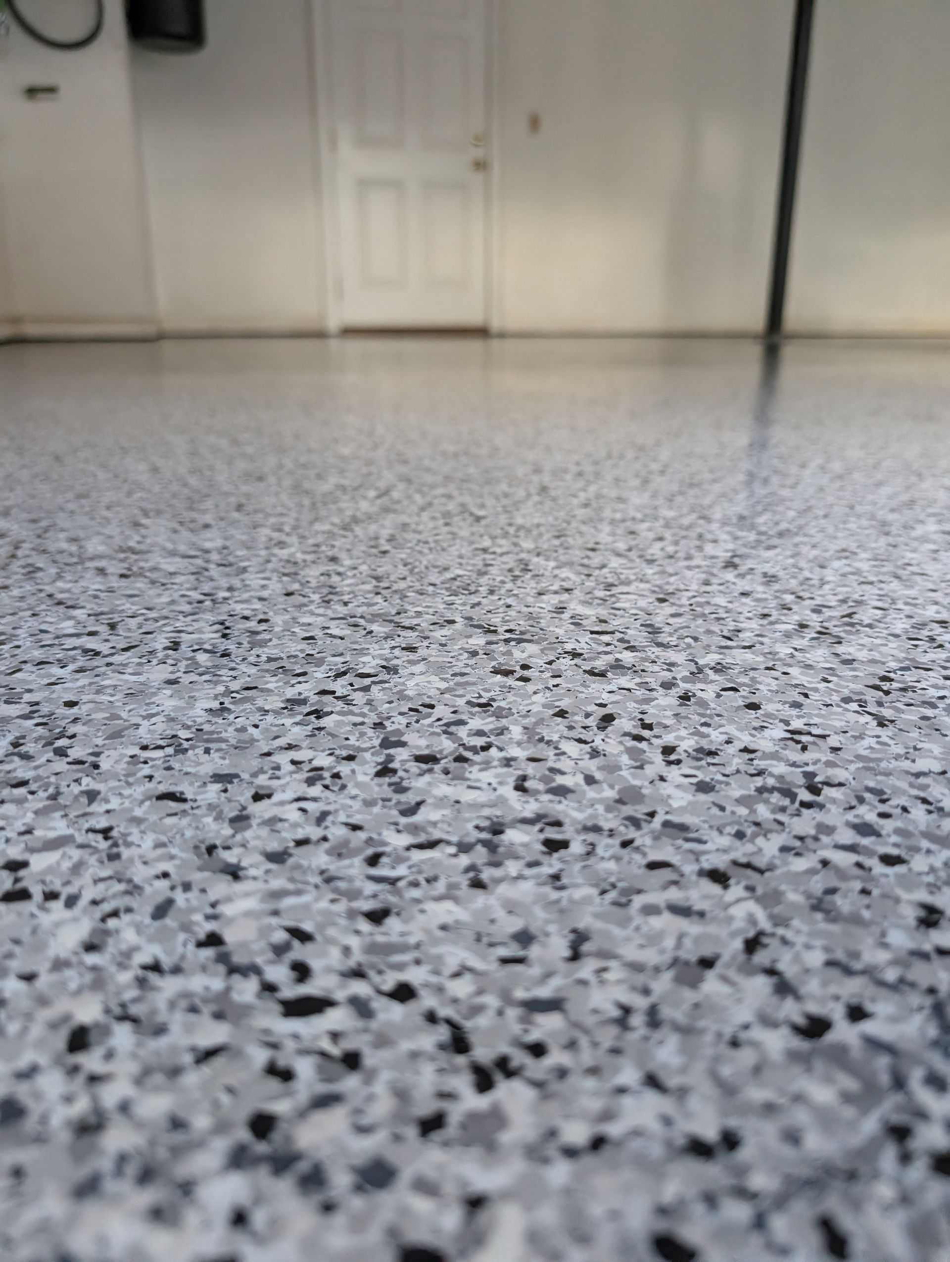 Low-angle view of a speckled gray floor leading to white doors in a plain hallway