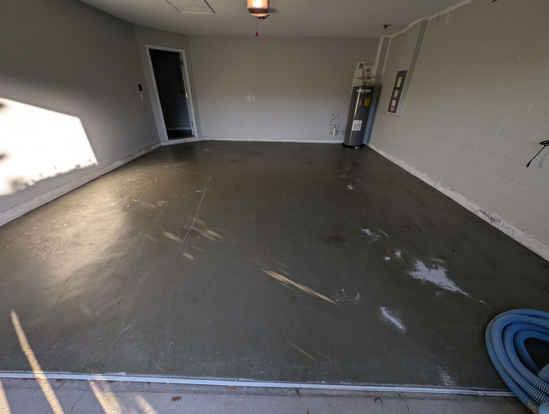 Empty garage with a gray concrete floor, white walls, and an open door letting in sunlight.