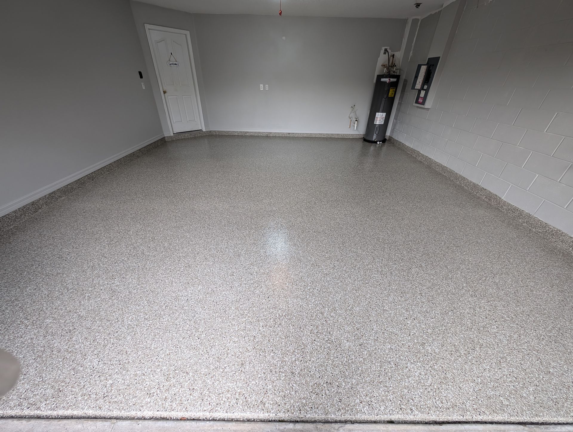 Empty gray garage with speckled floor, white door, and wall-mounted equipment on the right.